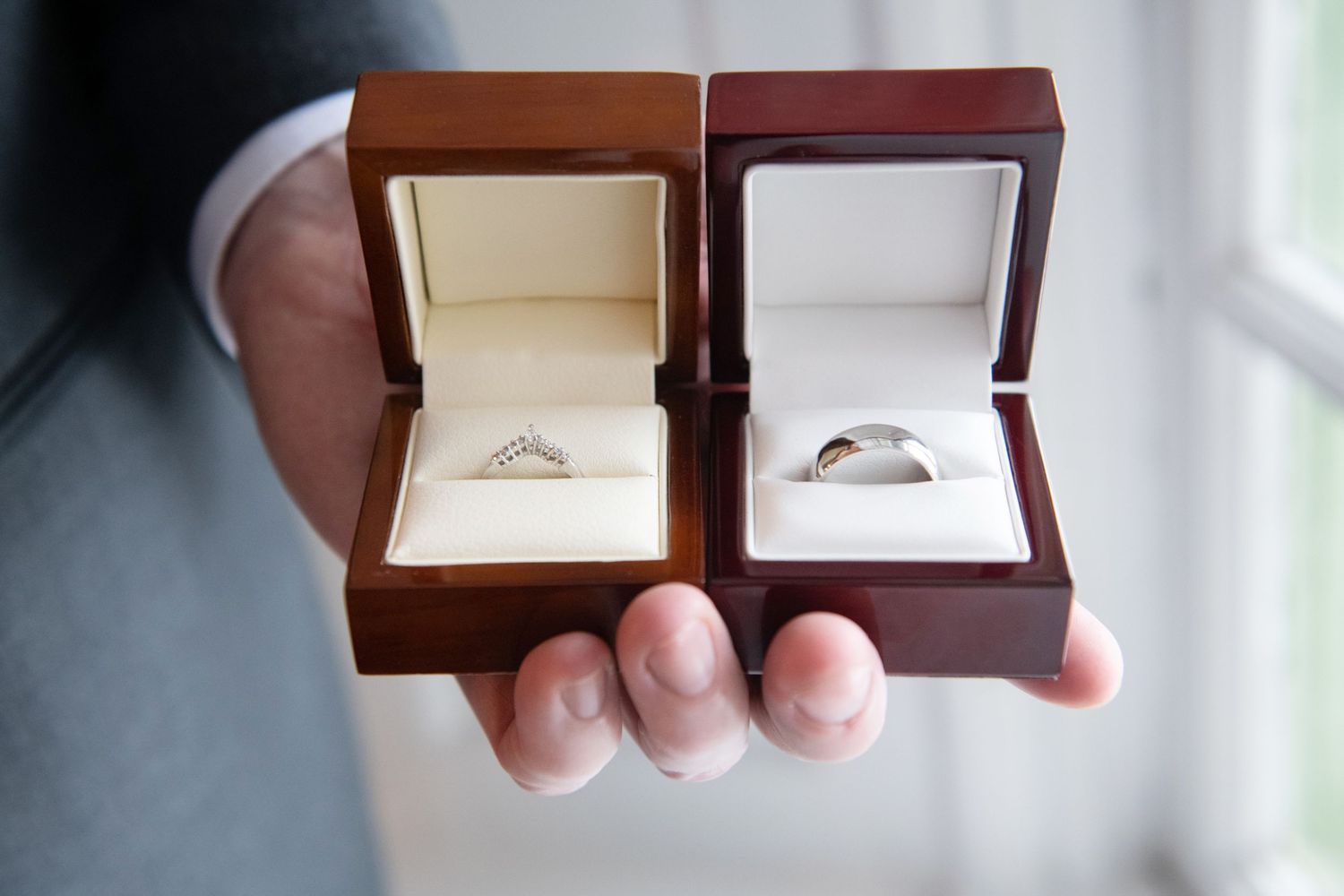 Two wooden ring boxes are held side by side showing their open lids and interior display cushions.