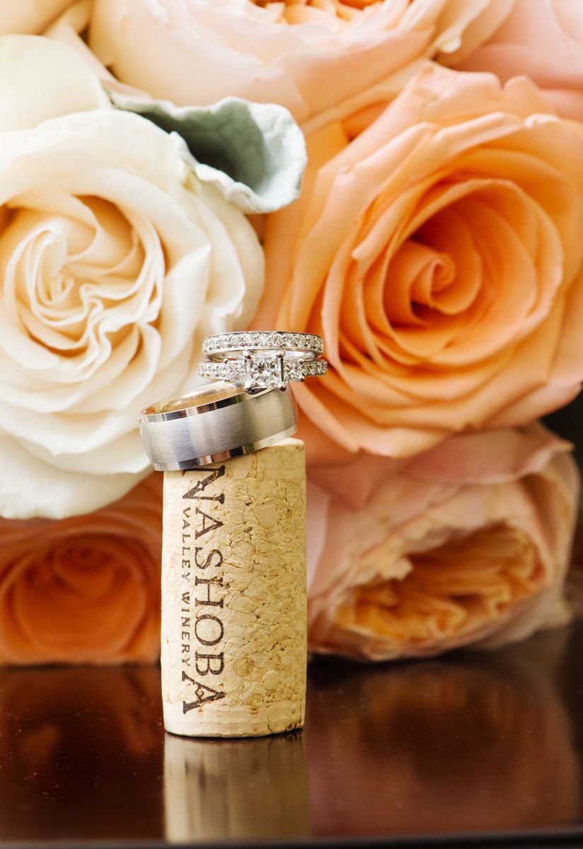 Wine cork arrangement with peach and white roses in soft focus background creates an elegant wedding detail photograph.