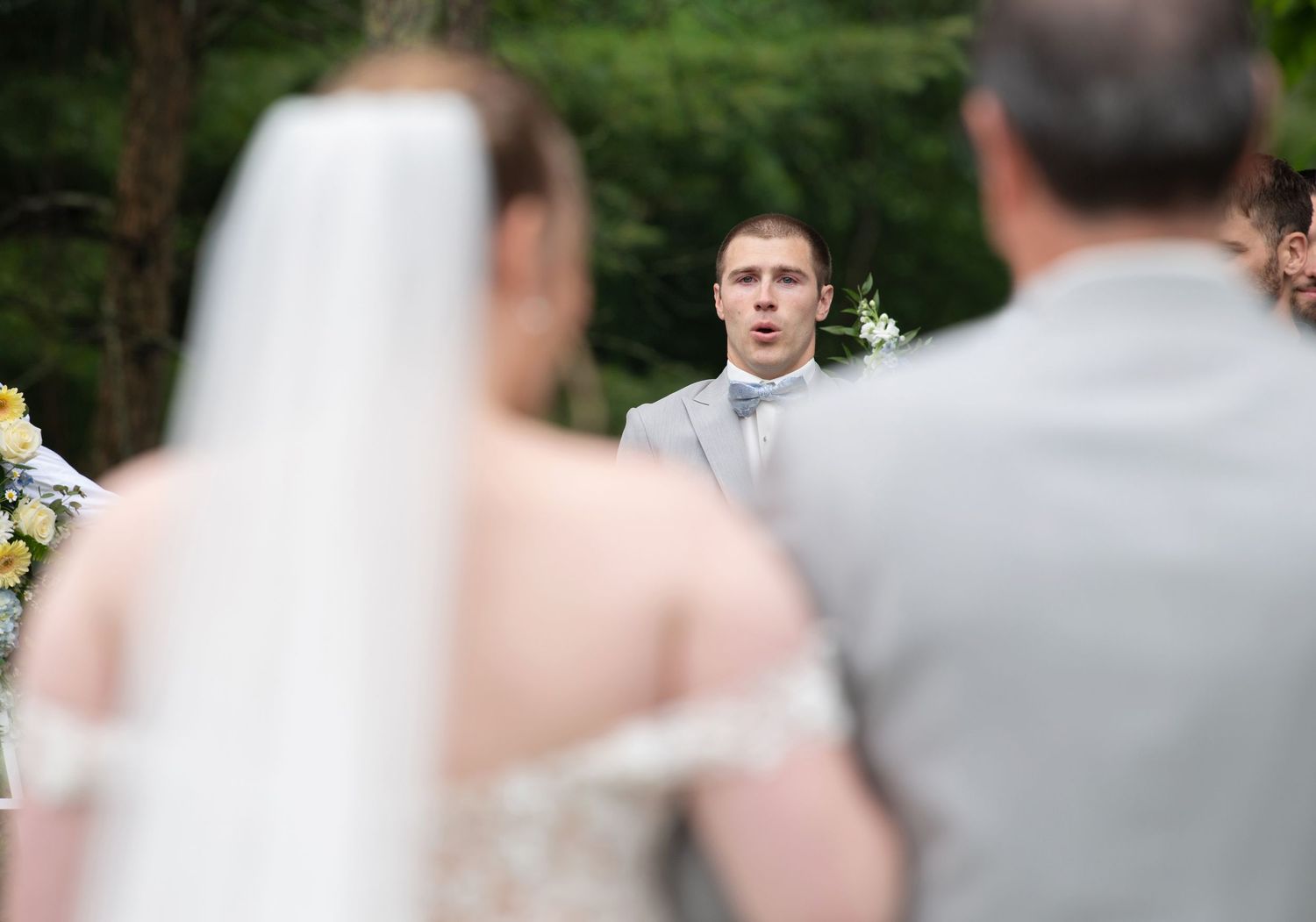 A wedding party stands in an outdoor garden setting surrounded by lush greenery during a summer celebration.