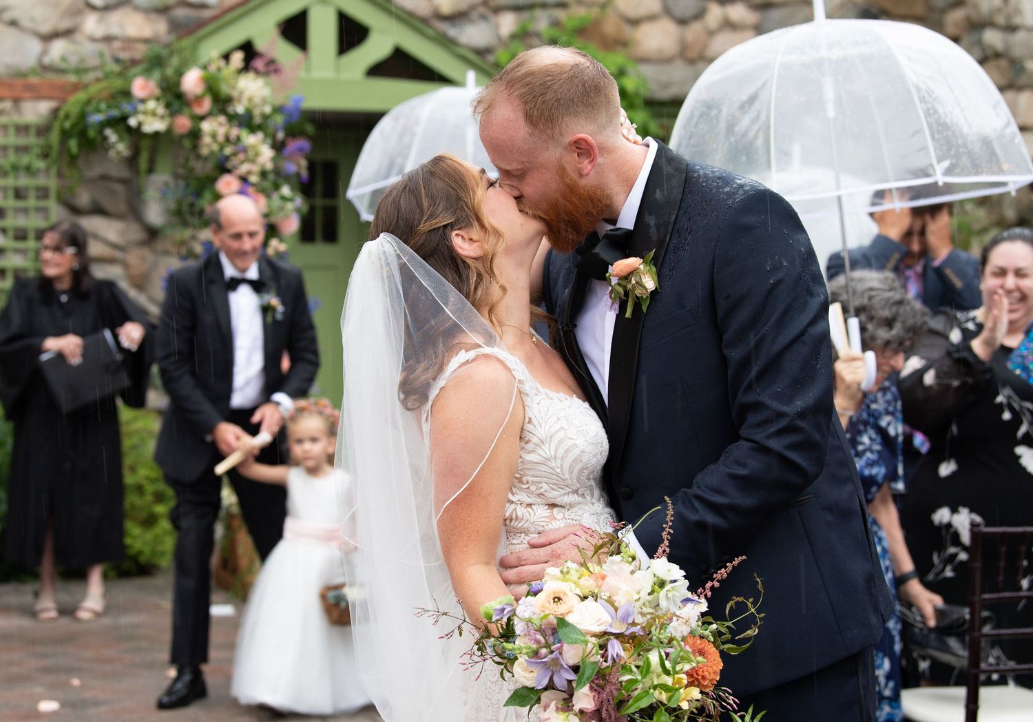 Newlyweds share romantic moment under white umbrella surrounded by floral arrangements.