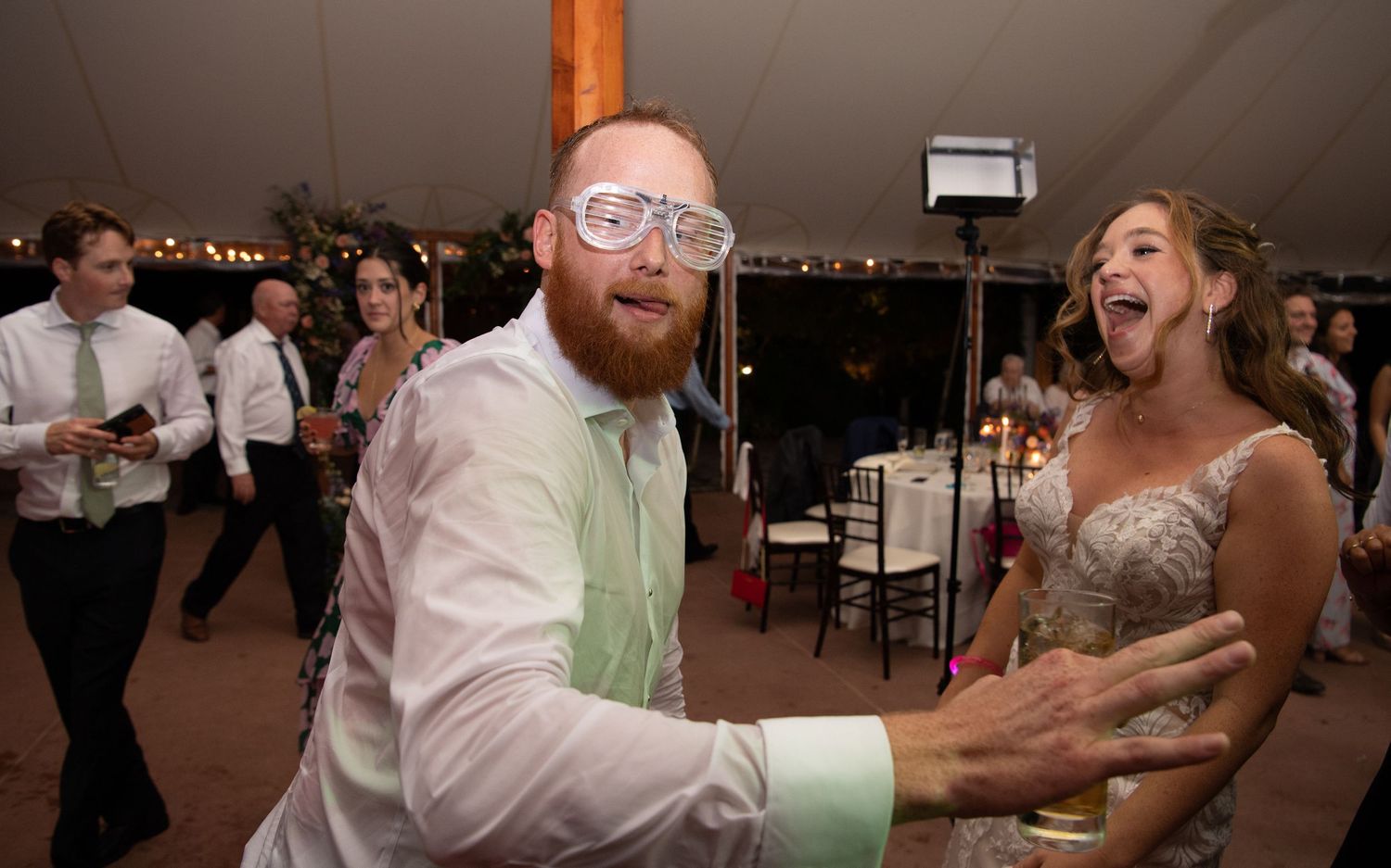 Reception celebration with guests dancing and laughing in festive indoor venue.
