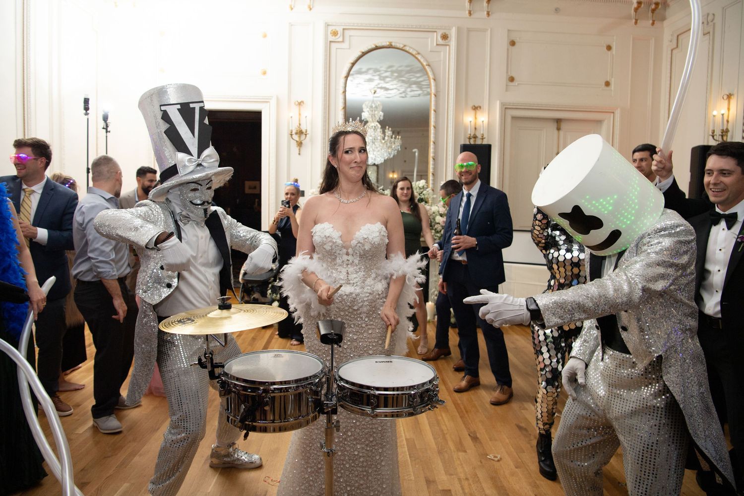 Bride in white gown poses with silver robot drummers performing at elegant wedding reception.