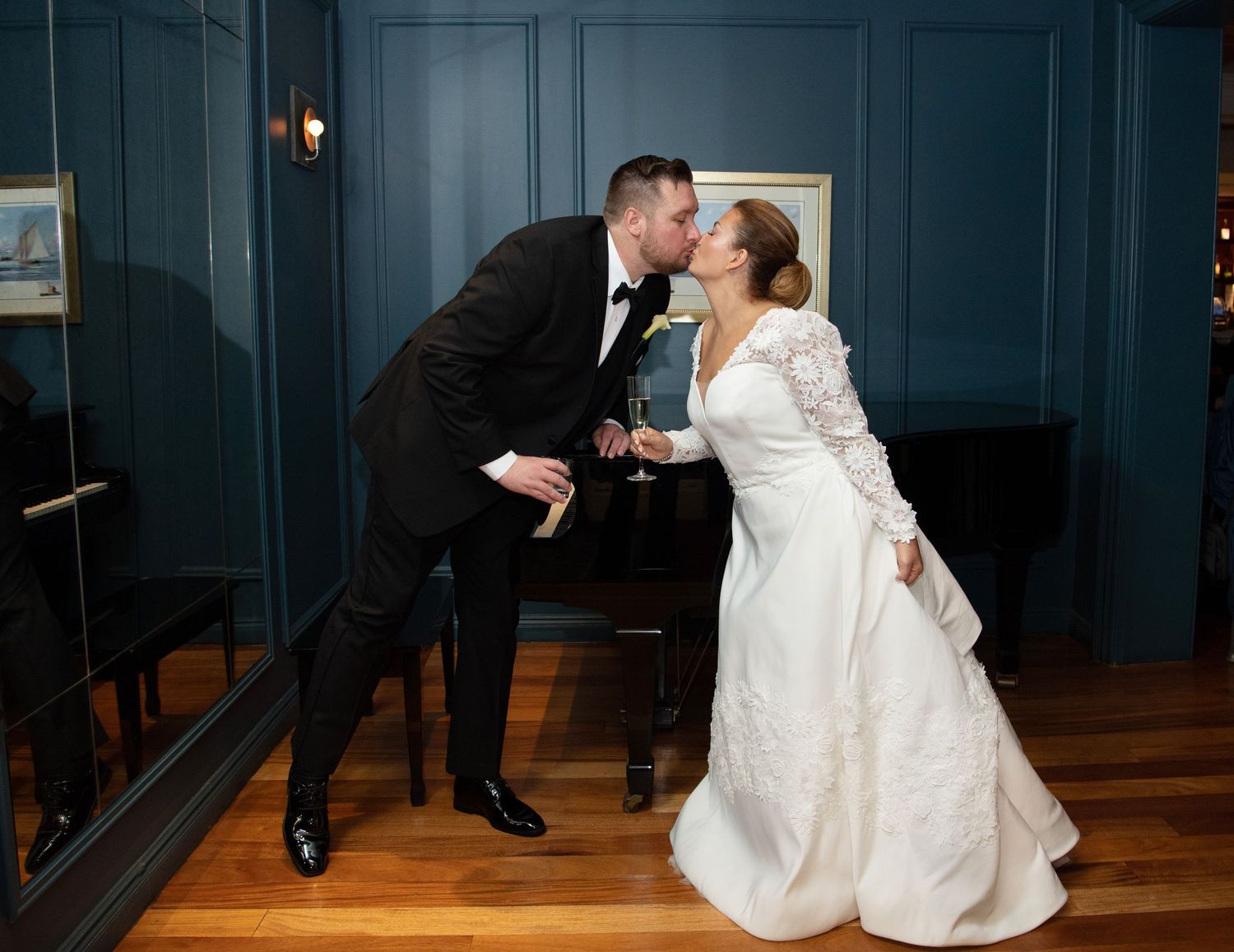 A couple in wedding attire shares a romantic dip kiss on a dark blue wooden paneled floor.