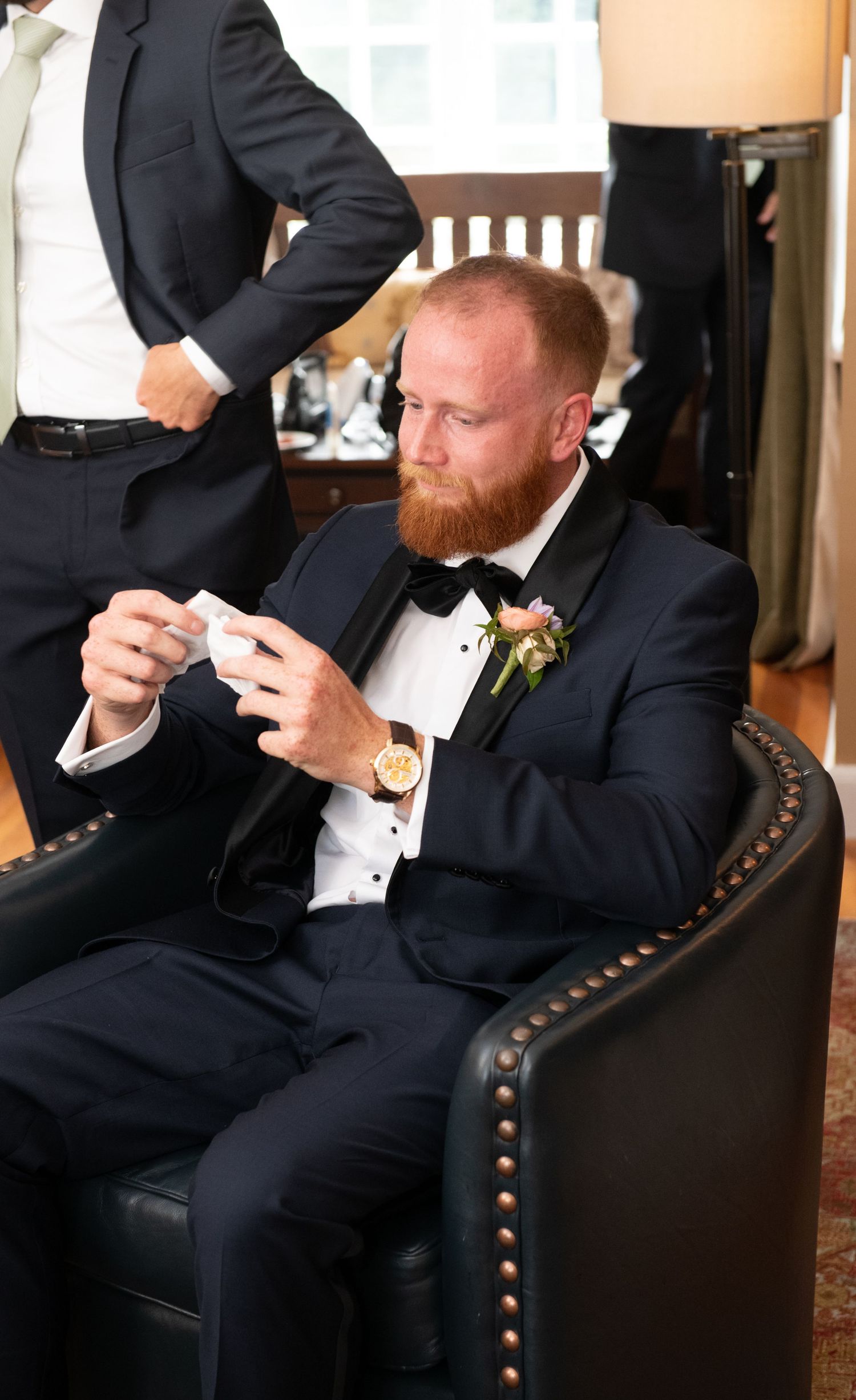 A person in a tuxedo reading a note while seated in an elegant leather chair.