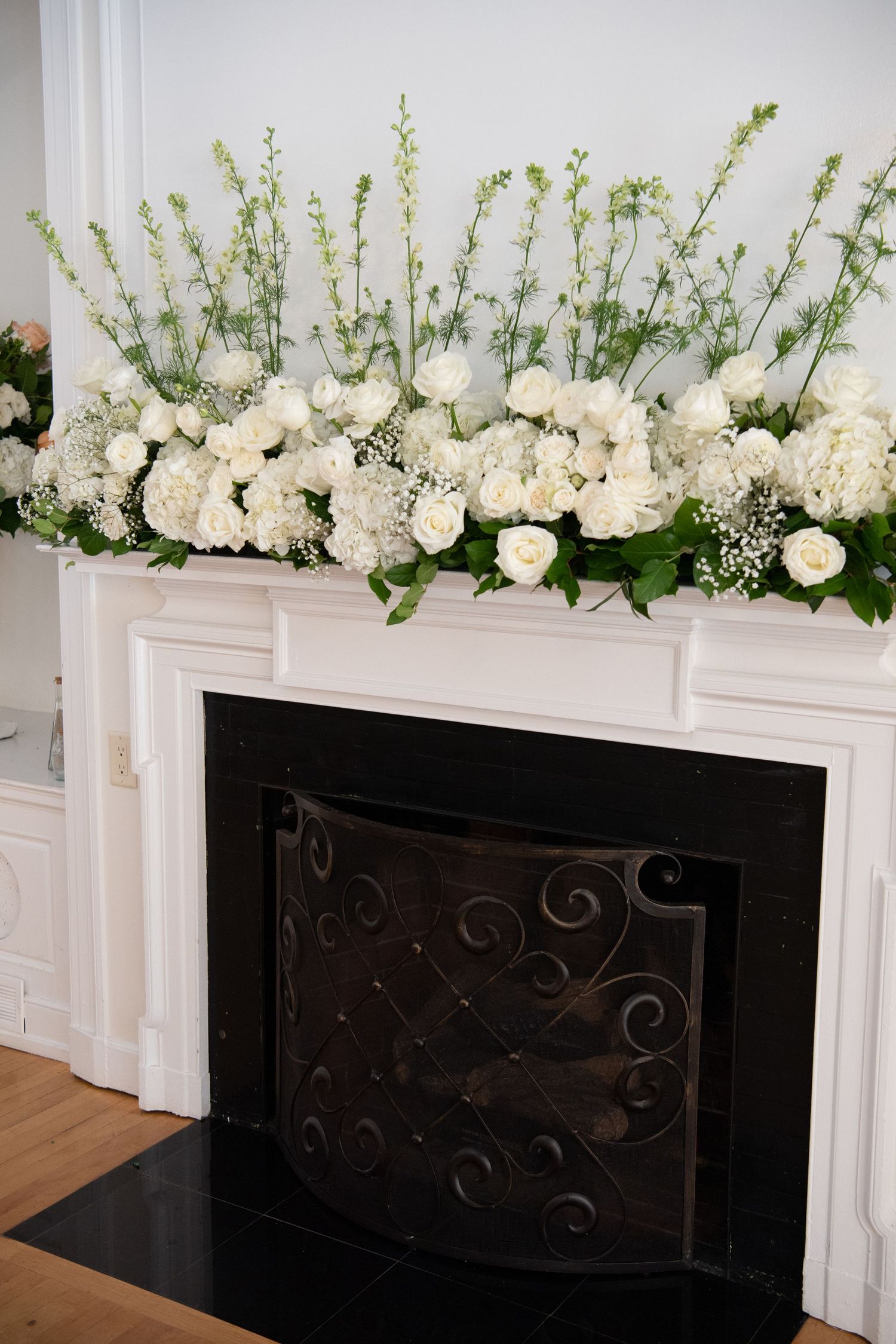 White floral arrangements with roses and greenery decorating a black fireplace mantel.