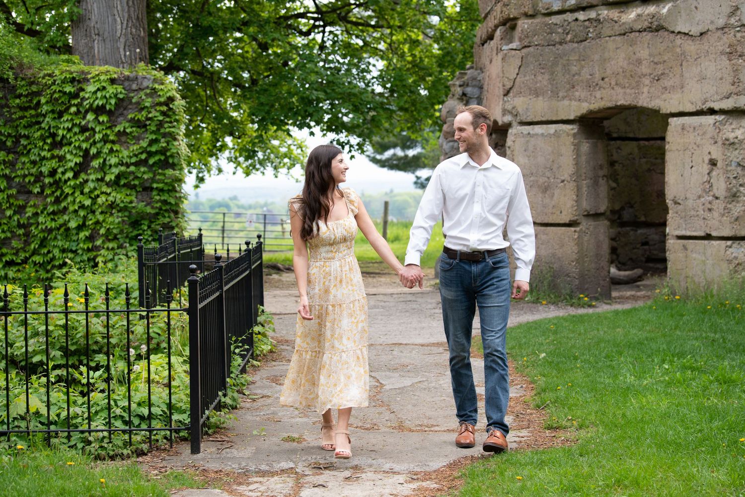 Couple in formal attire strolls along stone path in lush garden setting for romantic outdoor photos.