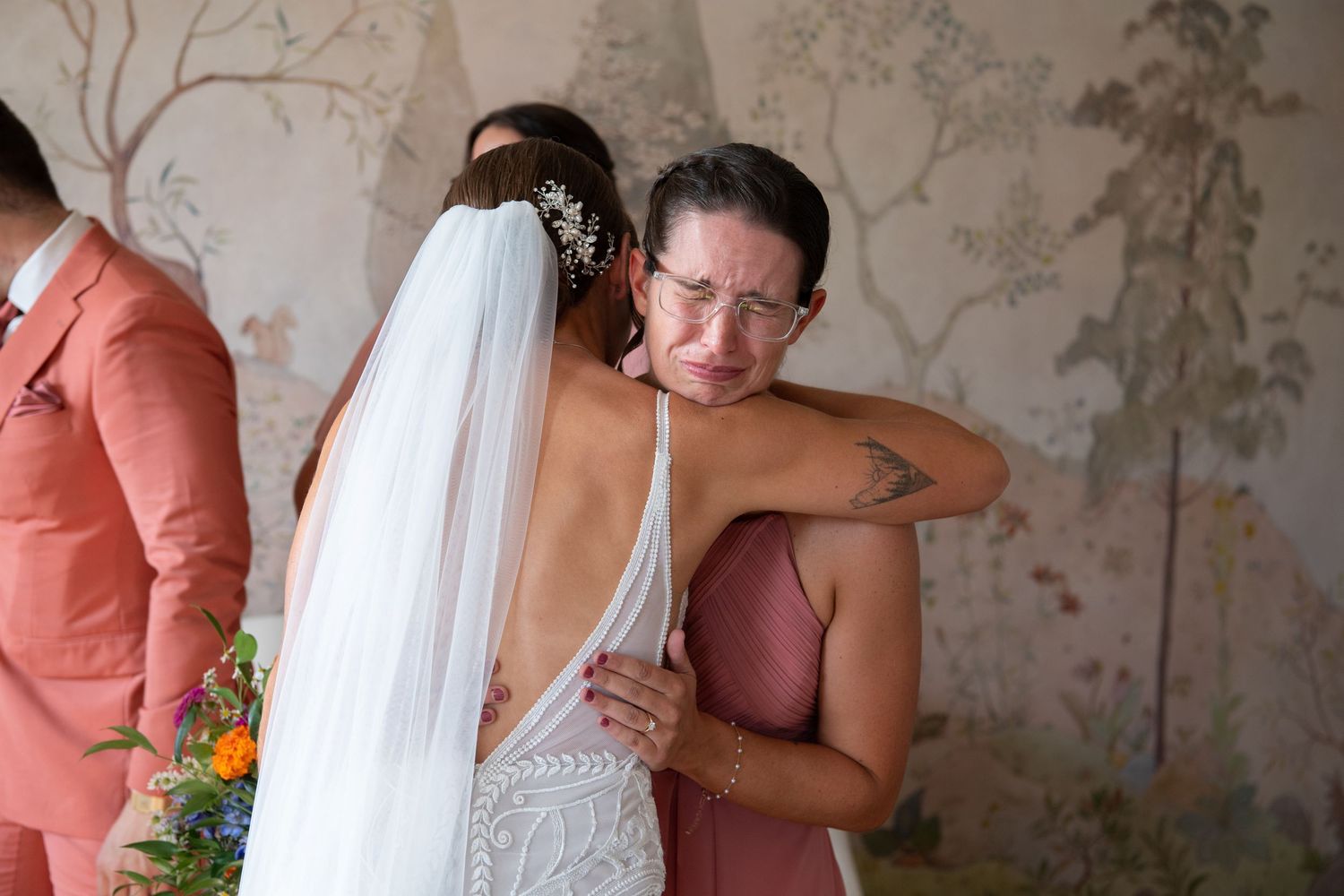 Emotional wedding scene showing tender embraces and heartfelt reactions in a room with floral wallpaper.