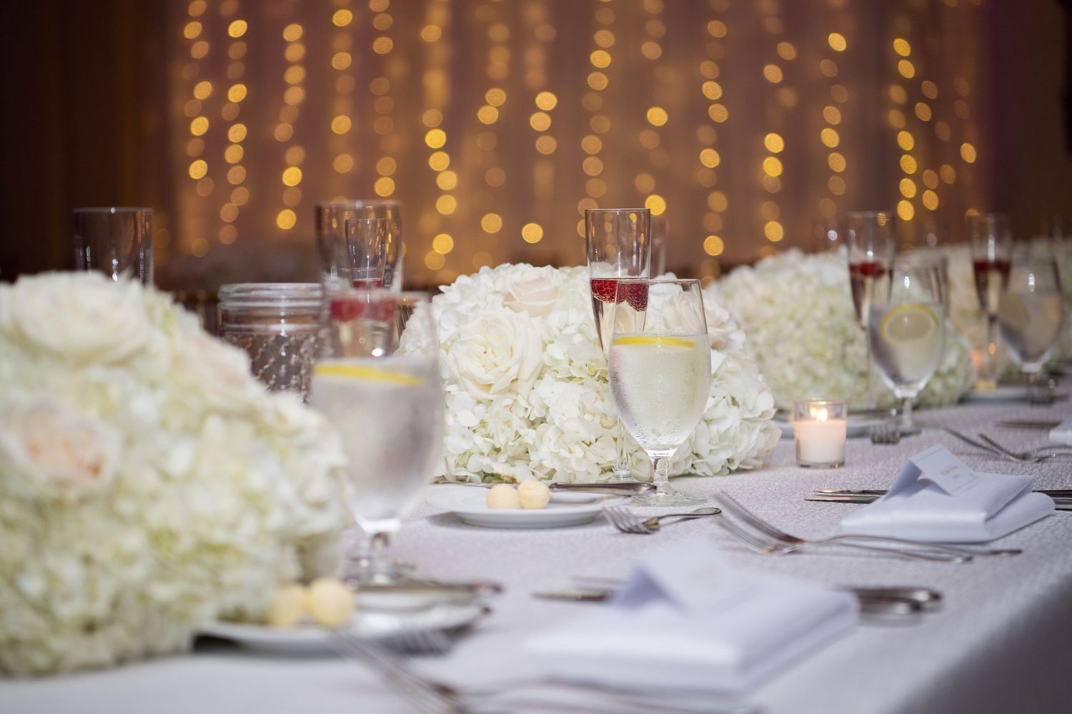 Wedding reception tables decorated with white hydrangea centerpieces and glowing candles create an elegant atmosphere.