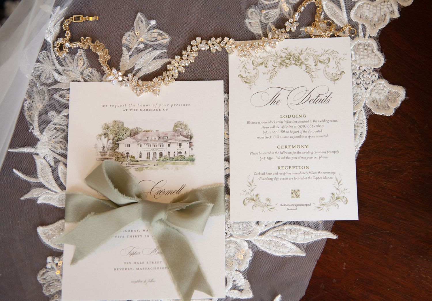 Elegant wedding stationery suite with illustrated venue card, sage green ribbon, and ornate details on lace veil backdrop.