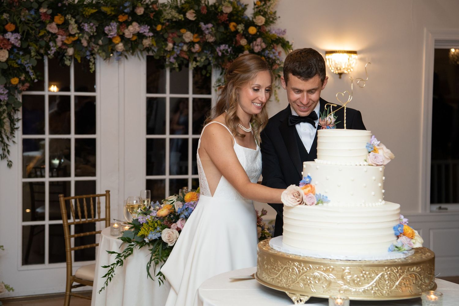 Newlyweds cut their elegant white and gold wedding cake together at their reception.