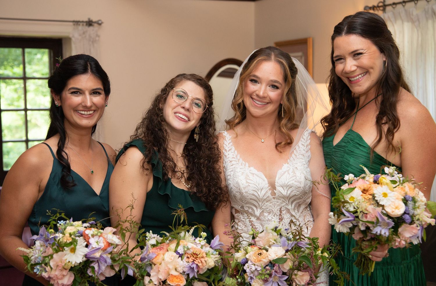 Bridal party wearing green dresses stands in a row holding colorful summer bouquets.