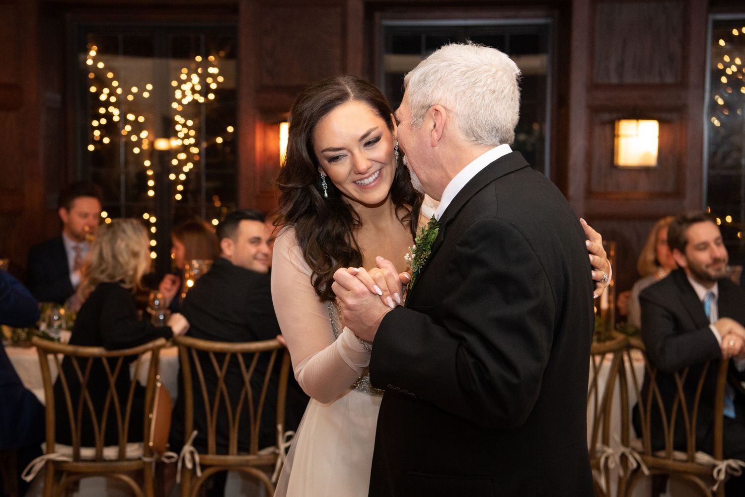 A couple shares a romantic dance moment during their wedding reception in a warmly lit venue with twinkling lights.