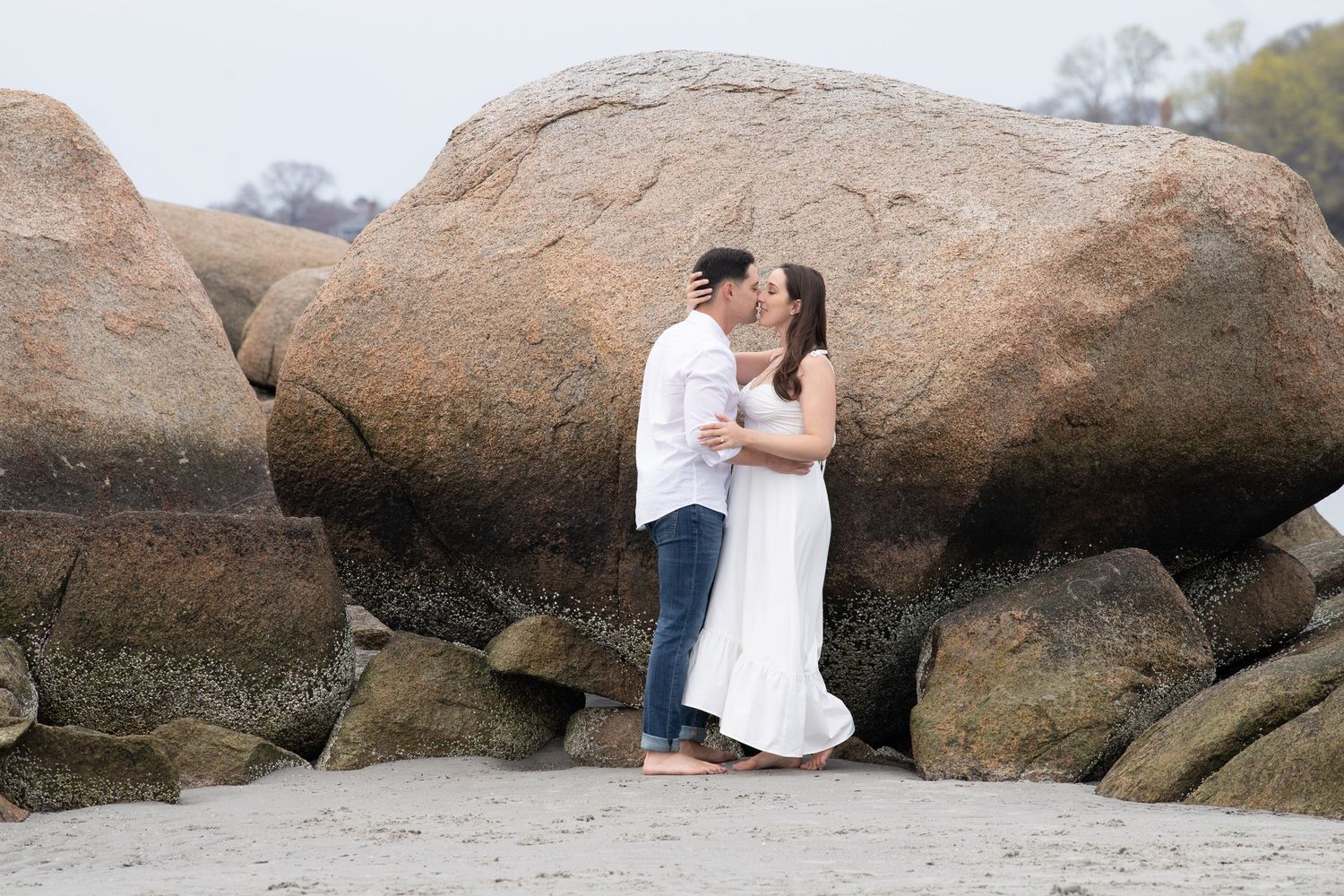 Romantic photoshoot among large coastal boulders at a scenic beach setting.