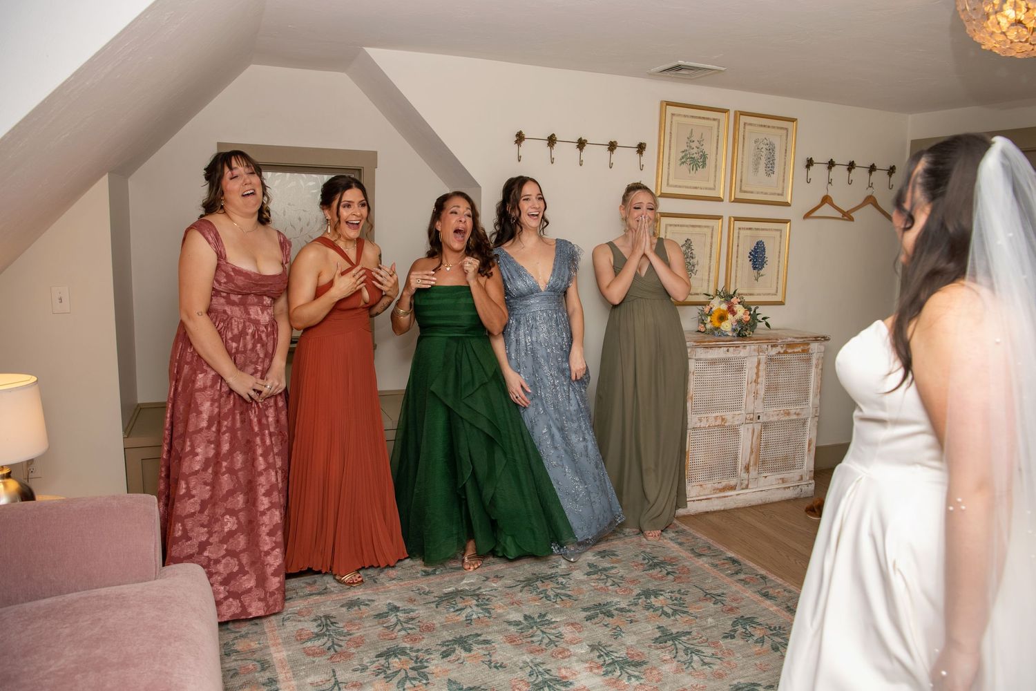 Bridal party in mismatched dresses of various colors including burgundy, rust, green and blue stand together in a boutique.