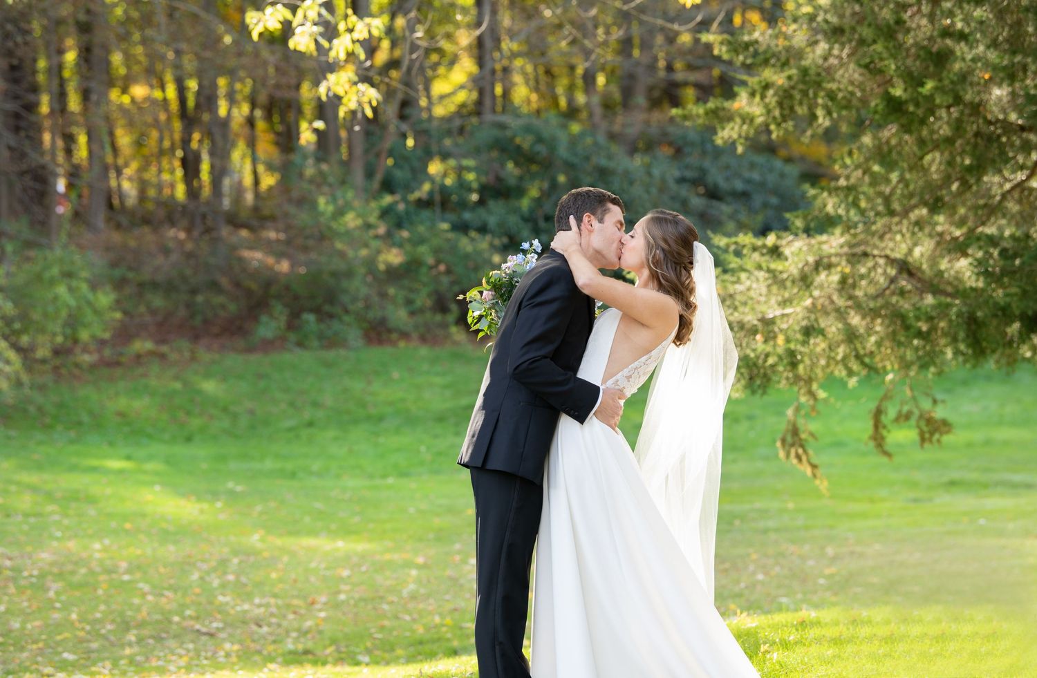 A romantic wedding couple embraces in a sunlit garden setting during their autumn wedding celebration.