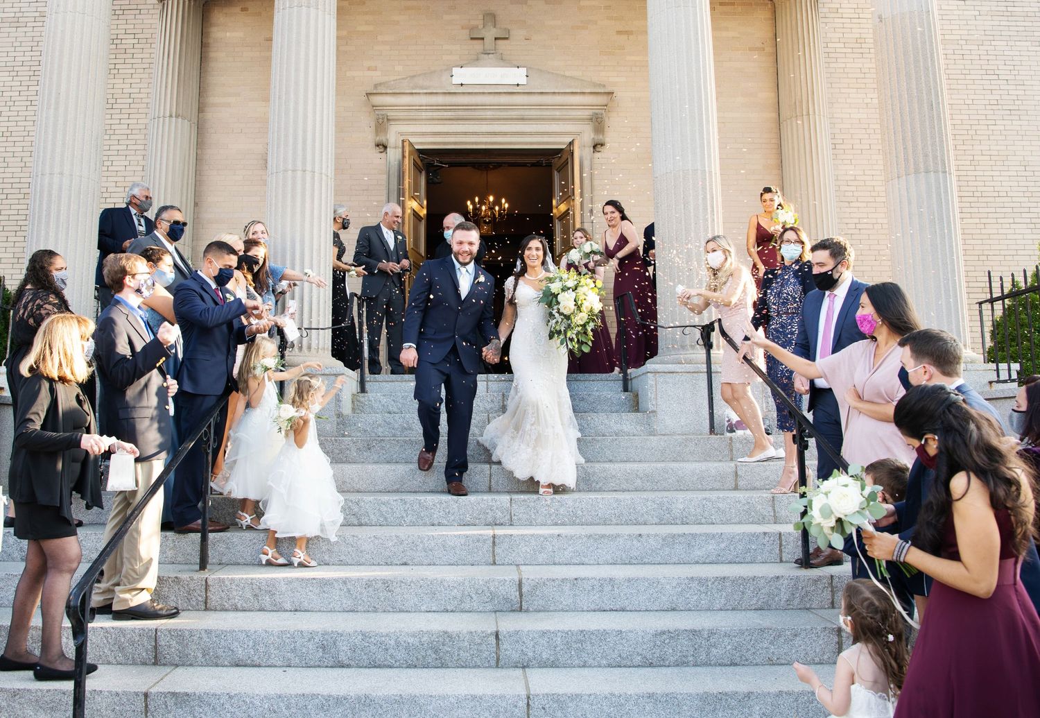 Wedding guests gather on grand stone steps of historic building after outdoor ceremony celebration.