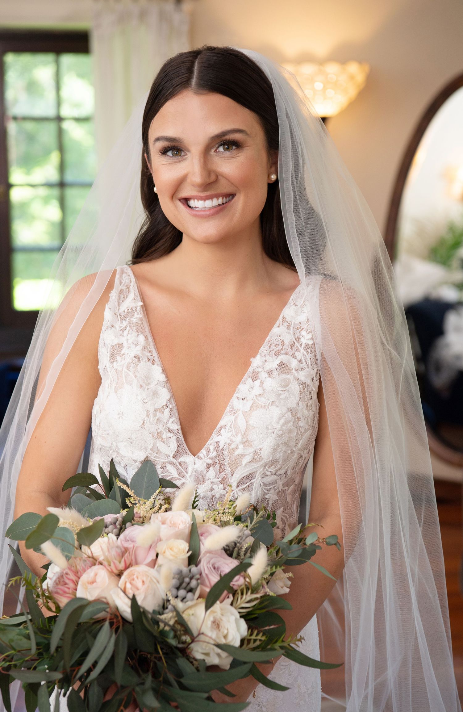 Bride wearing delicate lace V-neck wedding gown and veil holds romantic bouquet of blush roses and eucalyptus. willowdale estate bride