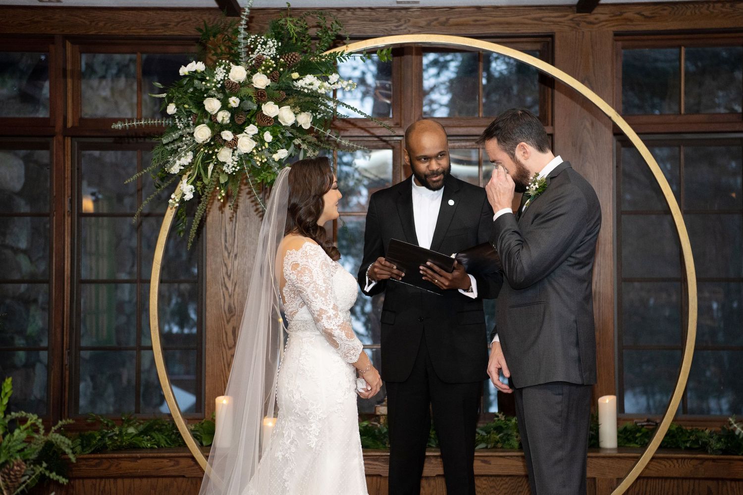 A wedding ceremony moment captured in front of a rustic wooden wall with white floral decorations.