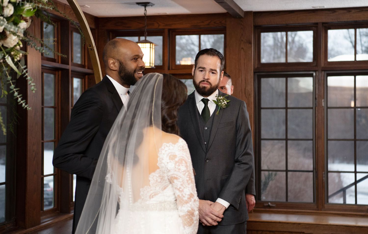 A bride and groom share a tender moment in a rustic wooden-framed room with large windows.