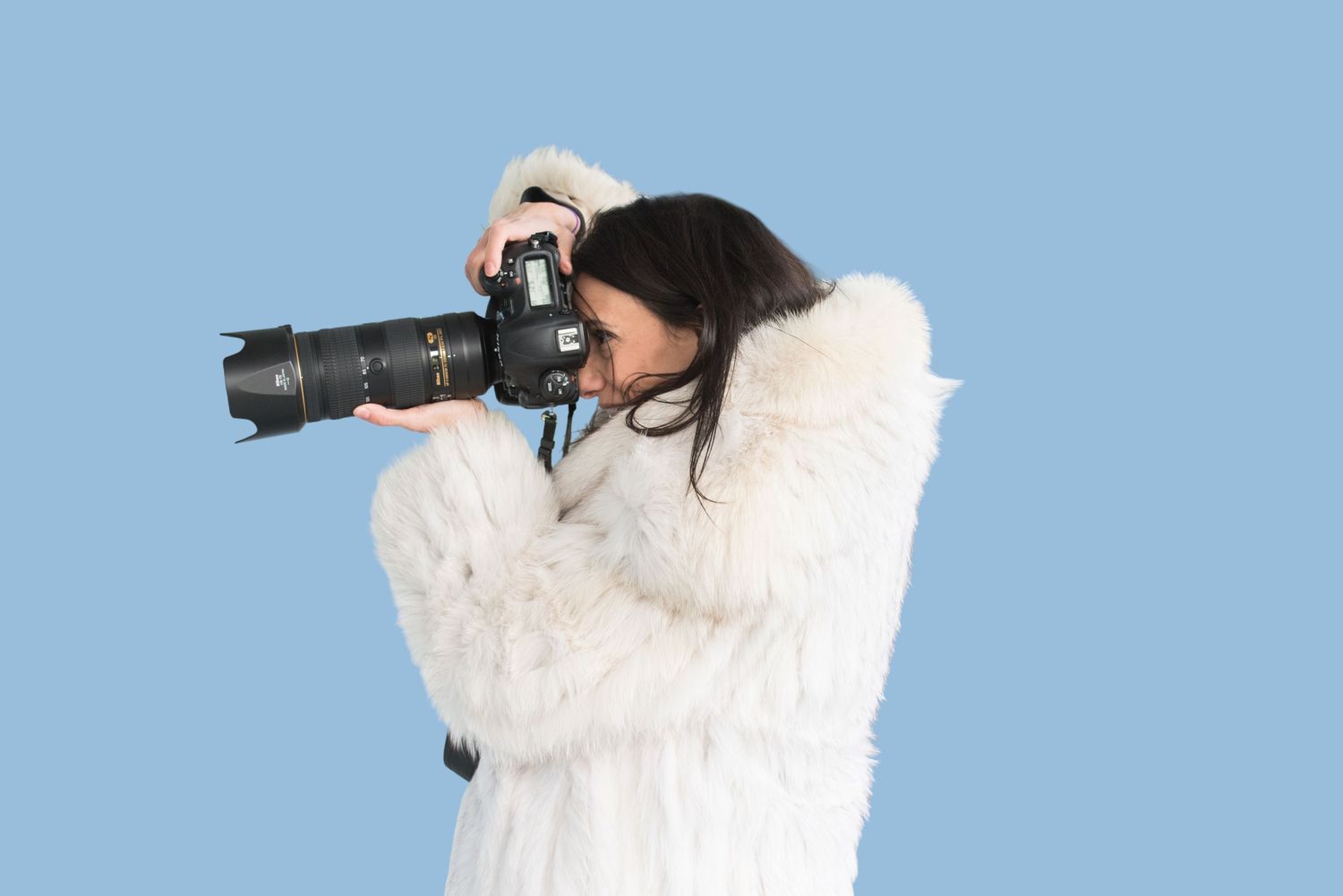 Photographer using a telephoto lens to capture wildlife against a bright blue sky background.