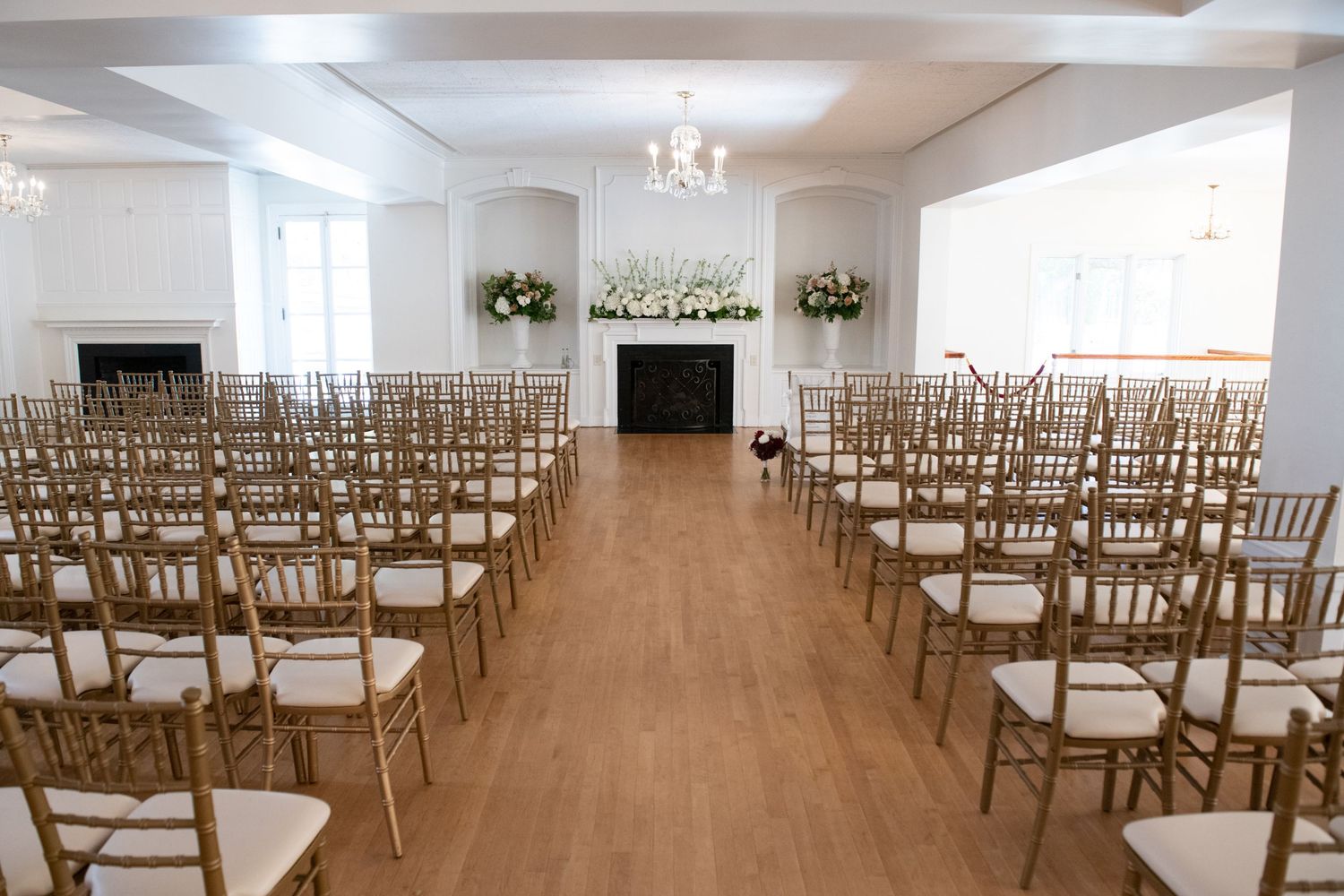 Elegant wedding ceremony venue with rows of gold chiavari chairs and white floral arrangements on pedestals.