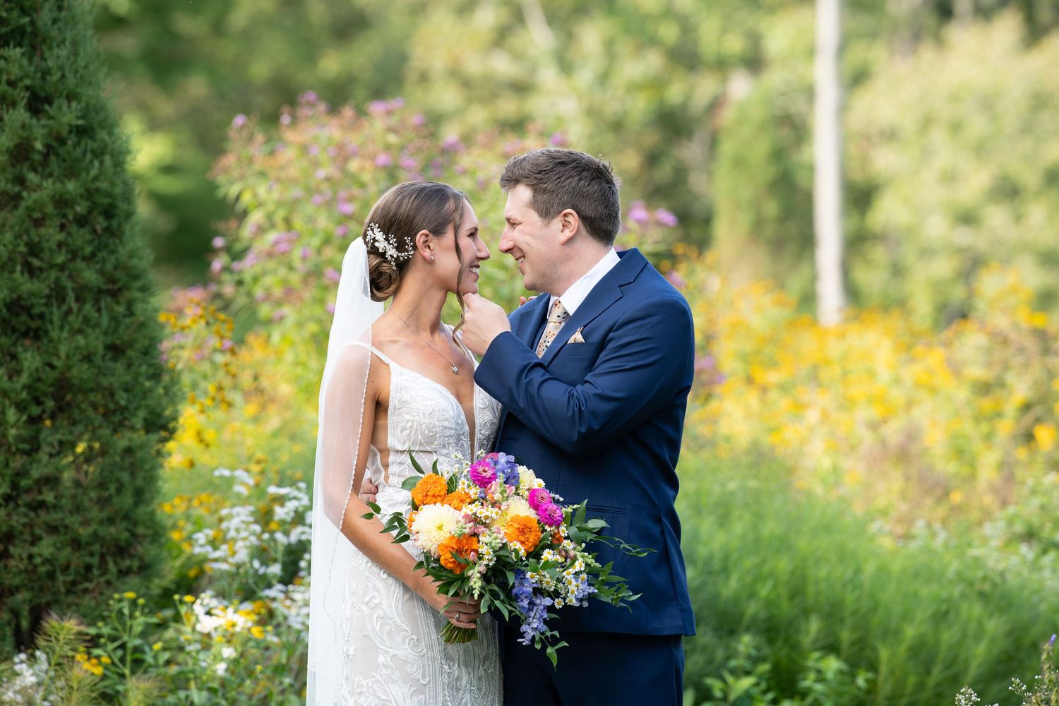 A couple shares a romantic moment in a garden filled with vibrant yellow wildflowers and lush greenery.