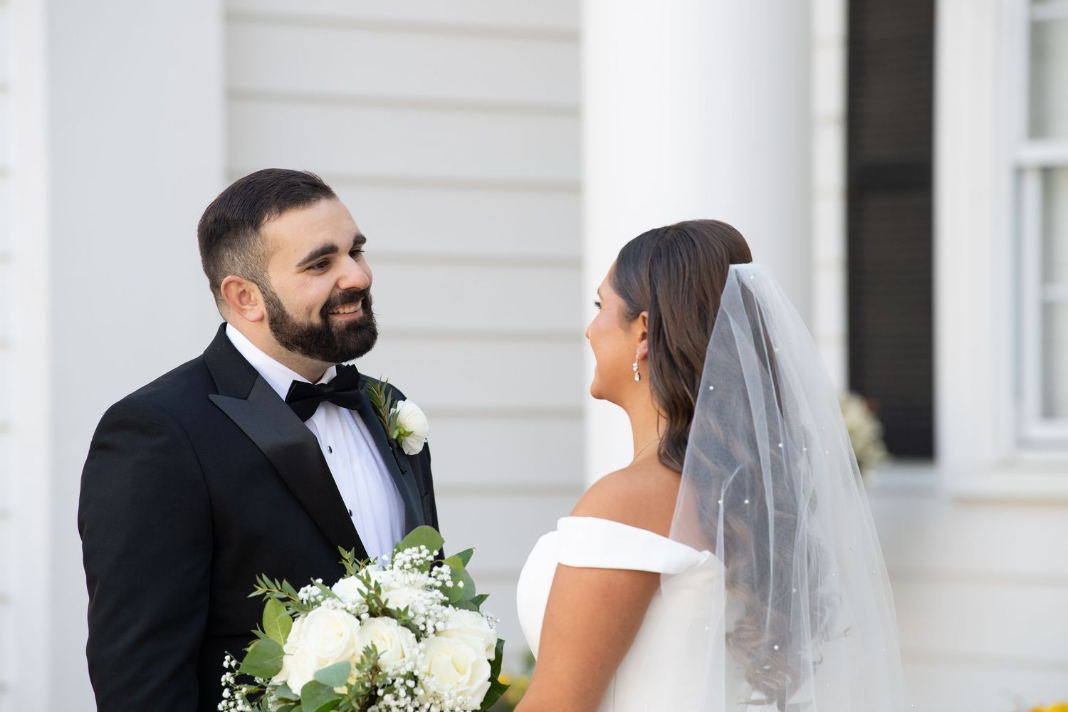A bride and groom share a romantic moment on their wedding day in front of white columns.