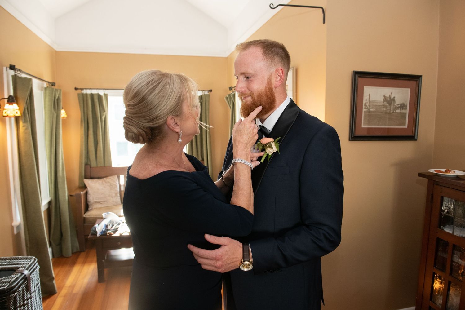 A tender moment shared between two people as a boutonniere is pinned onto a dark suit in a warmly lit room.