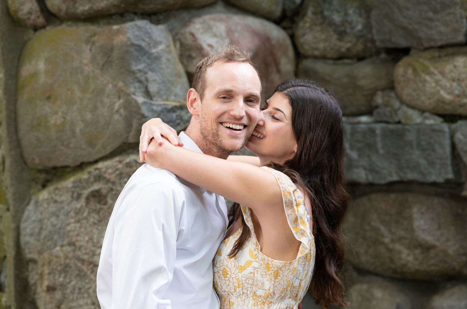 A romantic couple embraces and shares tender moments by a rustic stone wall.