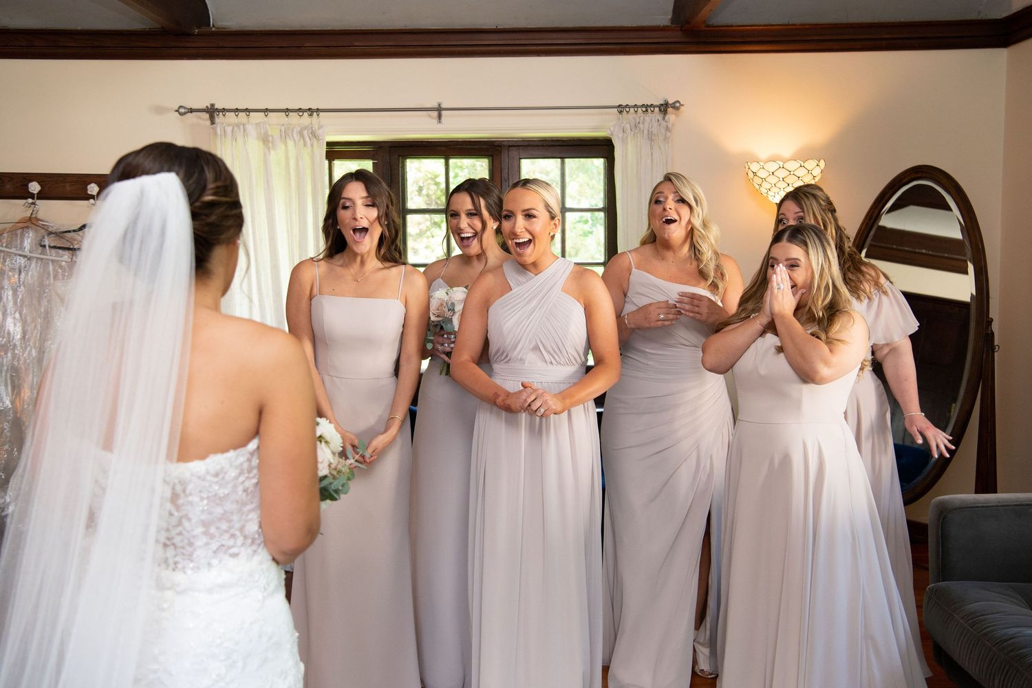 Bridesmaids in flowing gray dresses react emotionally during pre-wedding preparations in a cozy room. Willowdale Estate