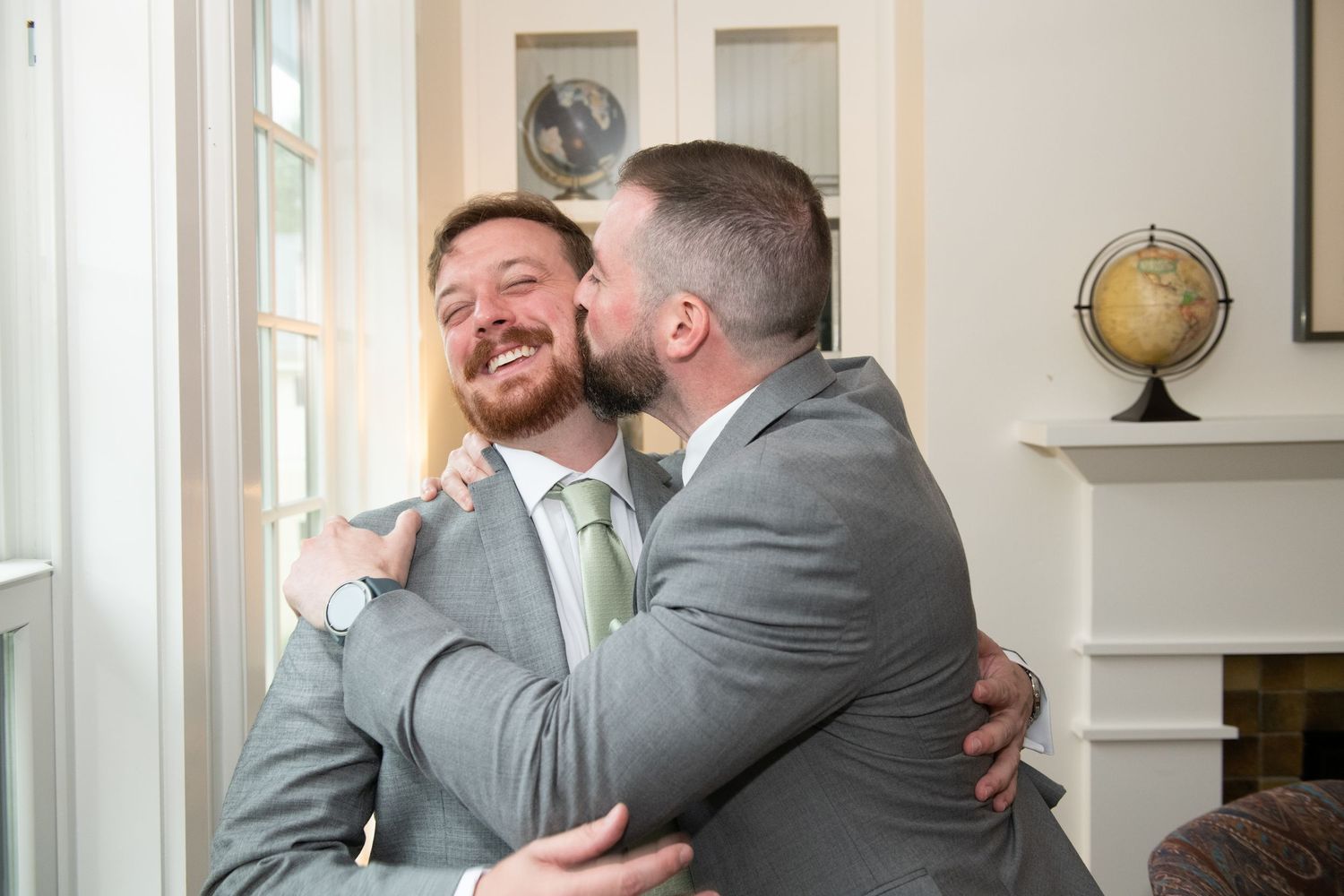 Groomsmen in grey suits share emotional embraces and reactions during pre-wedding preparations.