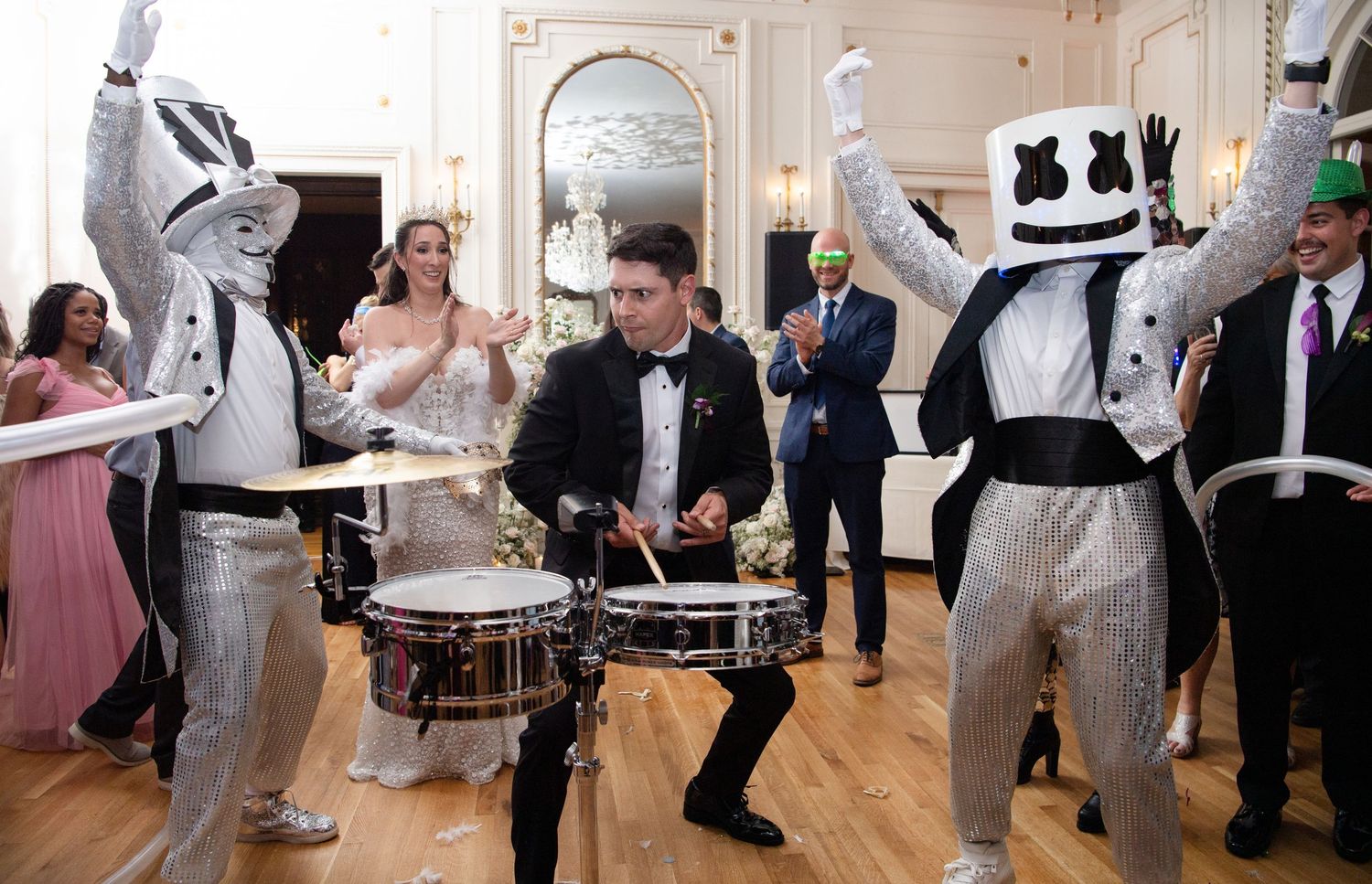 DJ Marshmello and silver-suited drummers perform at an elegant wedding reception with guests celebrating.