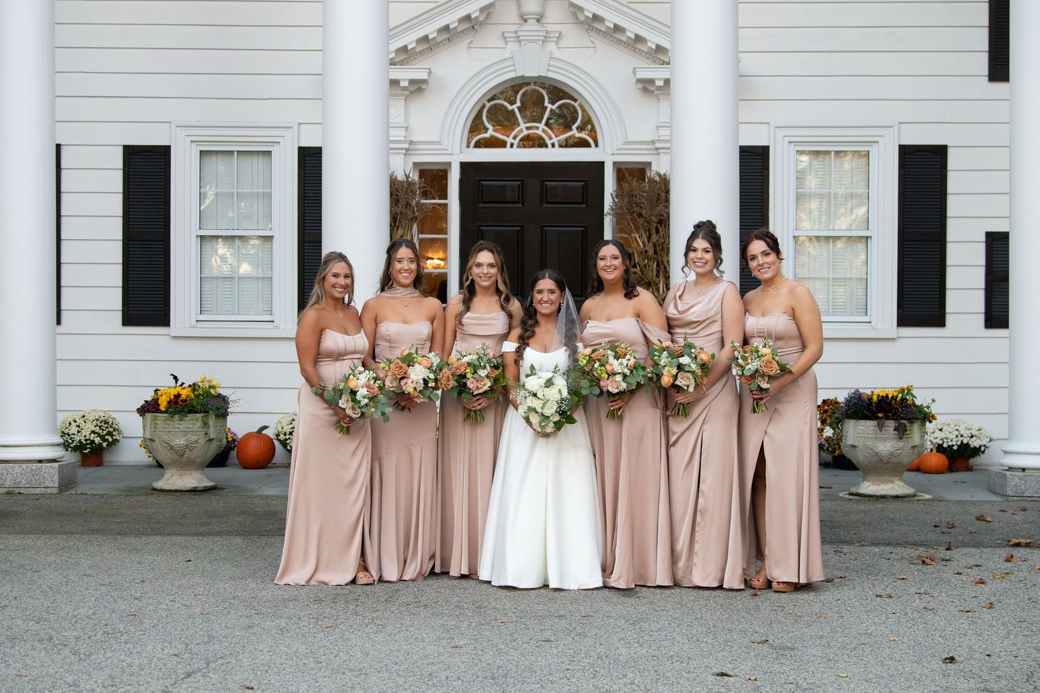 Wedding party in blush pink dresses posing in front of a white columned building.