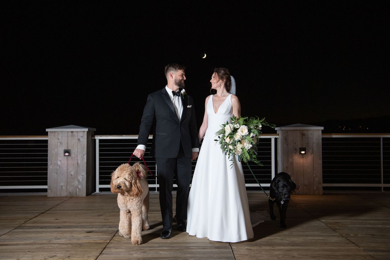 Romantic newlyweds share an intimate moment on an outdoor deck at night with subtle lighting ambiance.