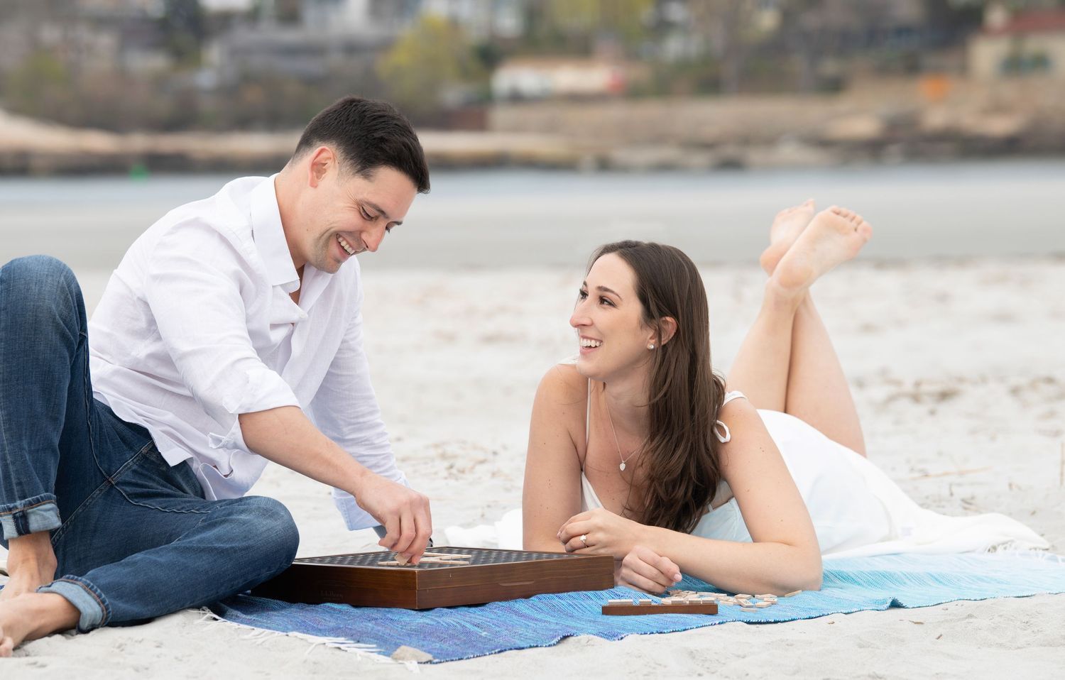 Young couple lies on a blanket at the beach sharing a romantic outdoor date together on a sunny day.
