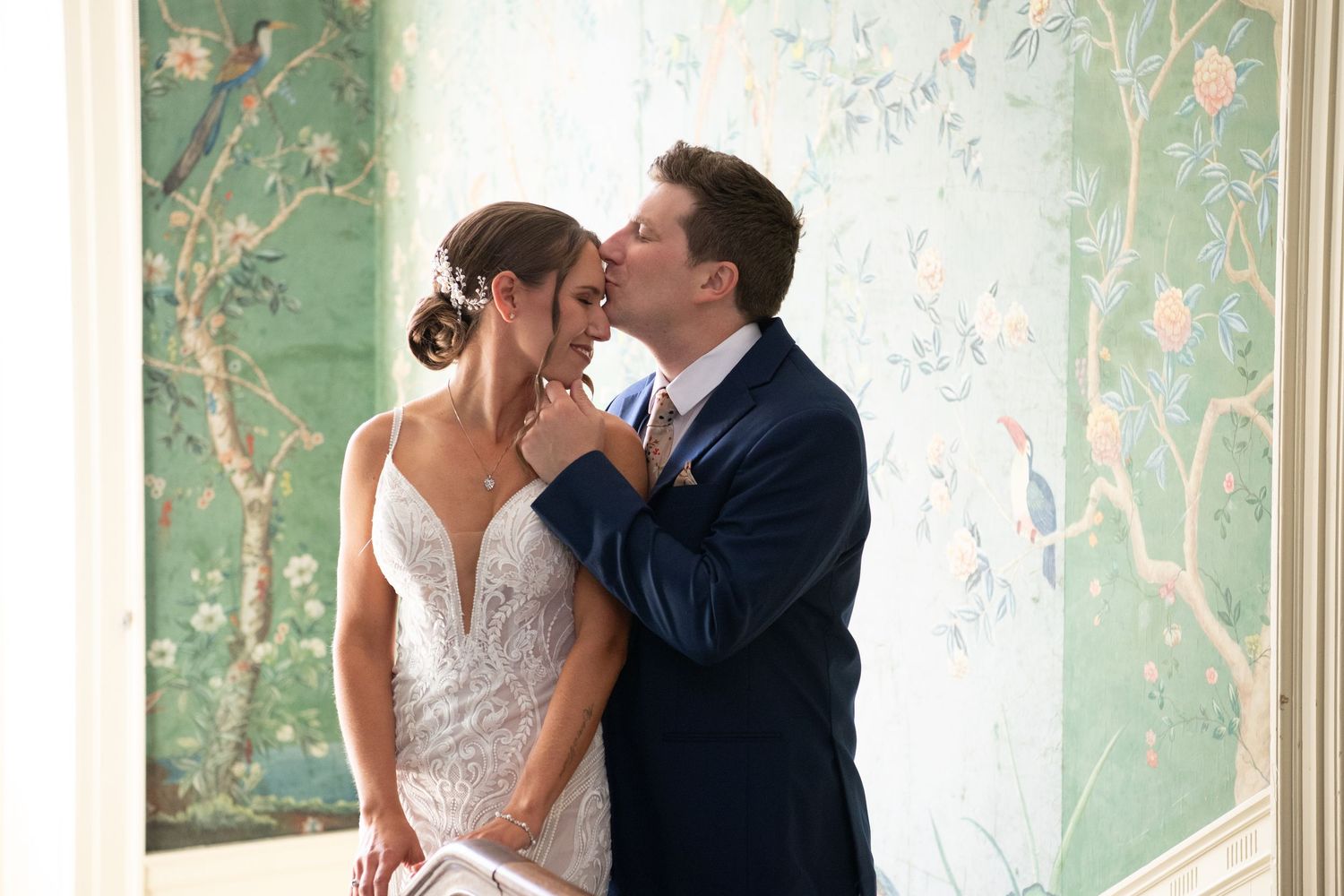 Wedding couple poses against elegant wallpapered interior with floral motifs.