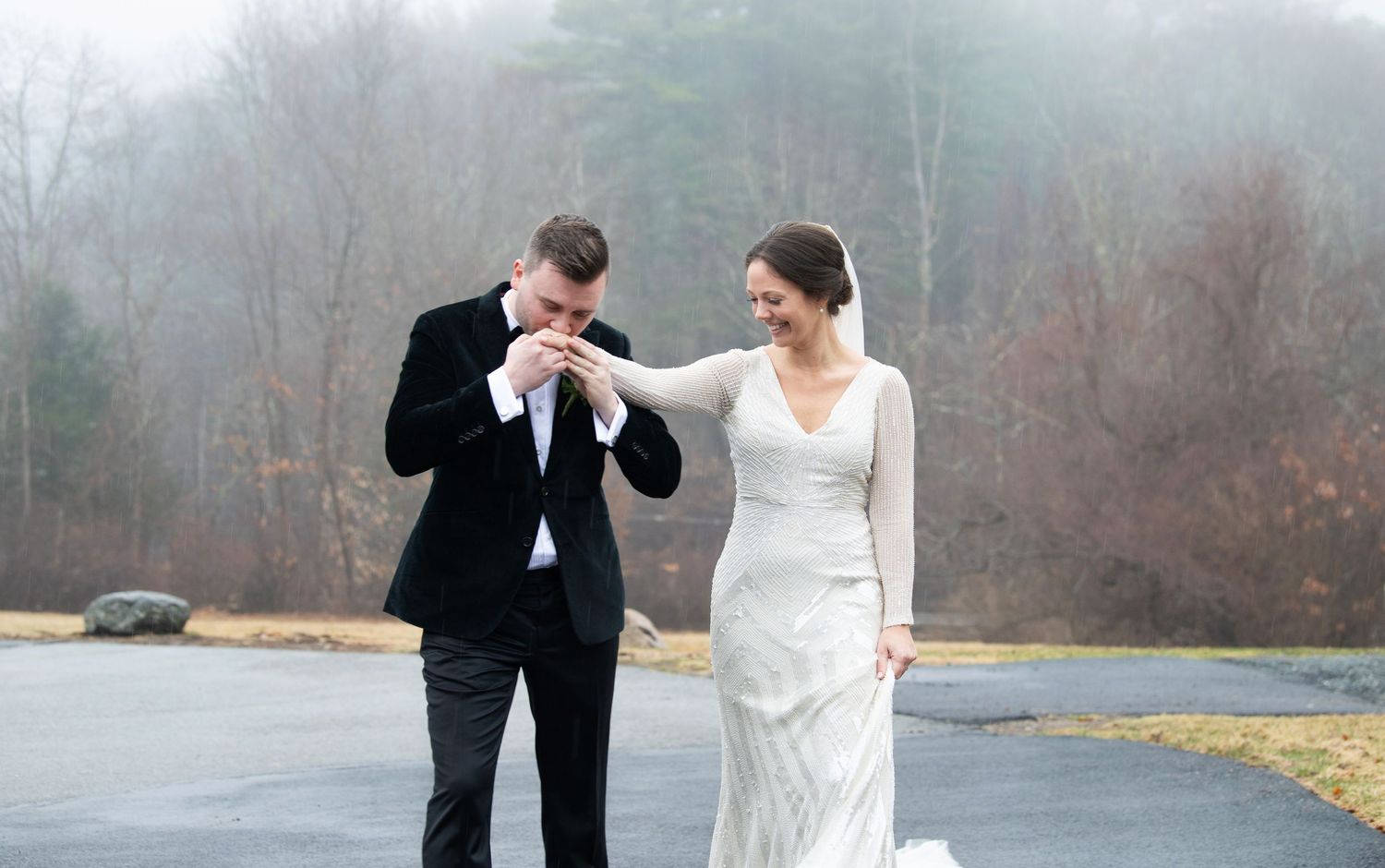 A couple in wedding attire stands on a foggy road in front of light fog covered trees during their intimate ceremony.