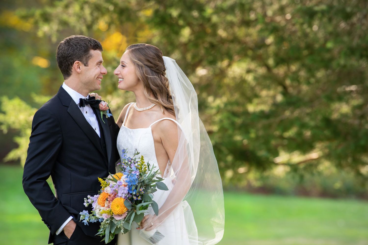 A couple in wedding attire share intimate moments in a lush garden setting with autumn foliage in the background.