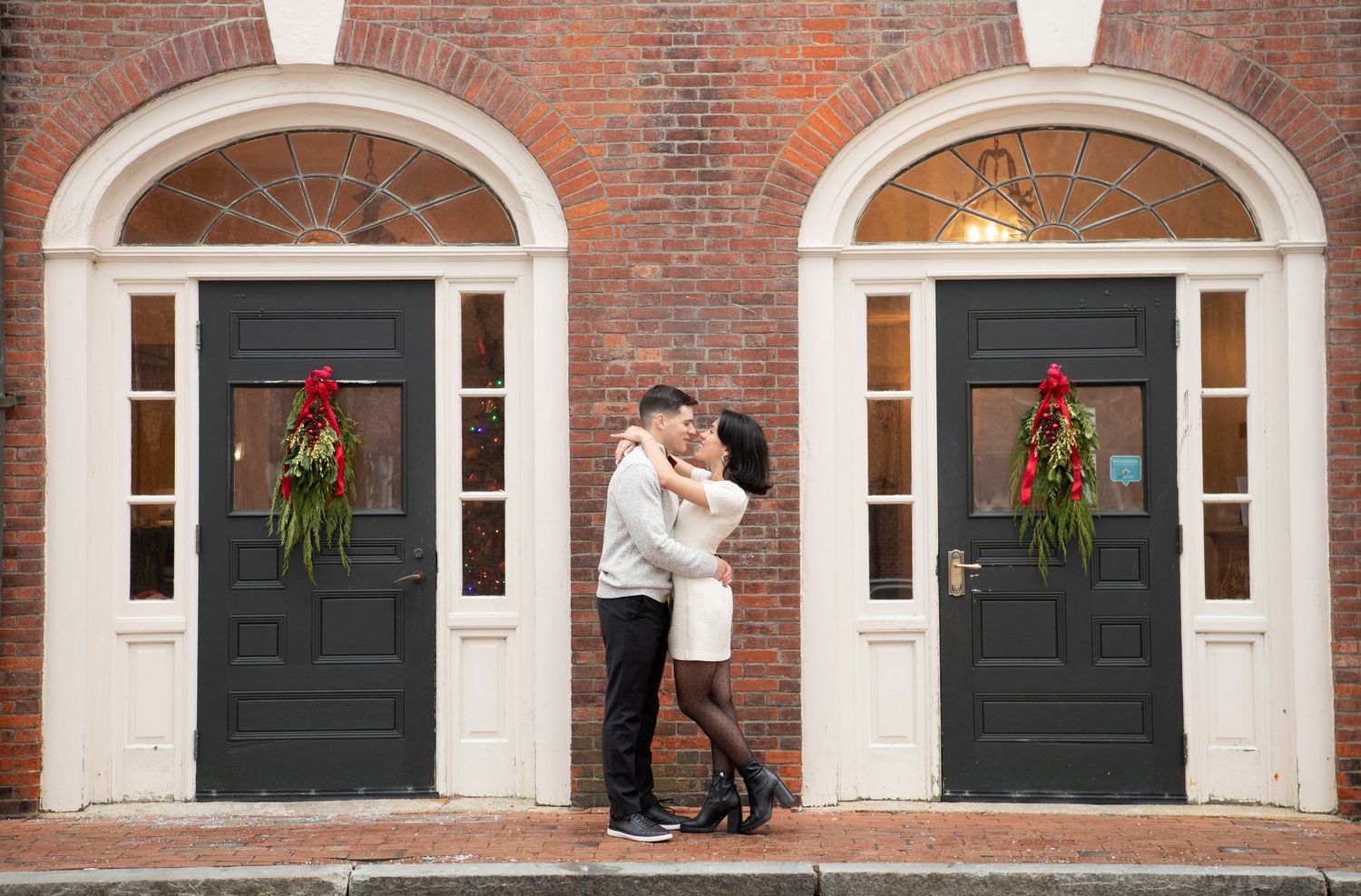 A sequence of black front doors with white arched frames against a red brick building decorated with holiday wreaths.
