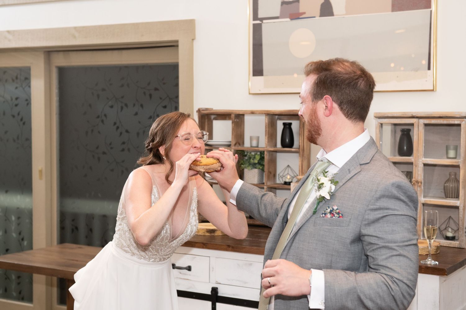 A couple shares cake during their wedding reception while laughing together.