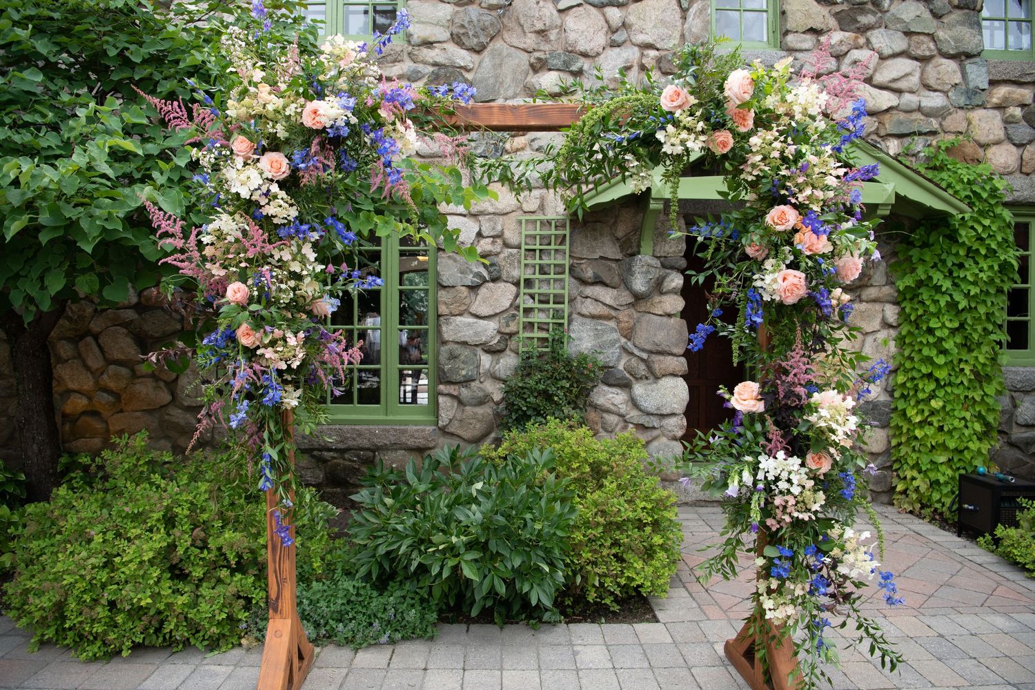 Beautiful floral arch with pink and purple blooms against a stone wall with green door and windows.