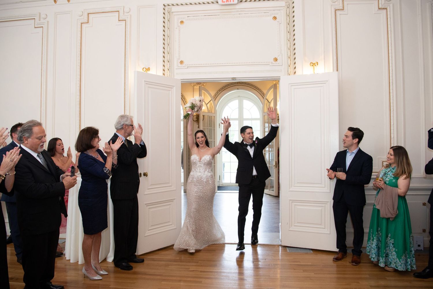 Newlywed couple makes grand entrance at elegant ballroom wedding reception, guests applauding in formal attire.