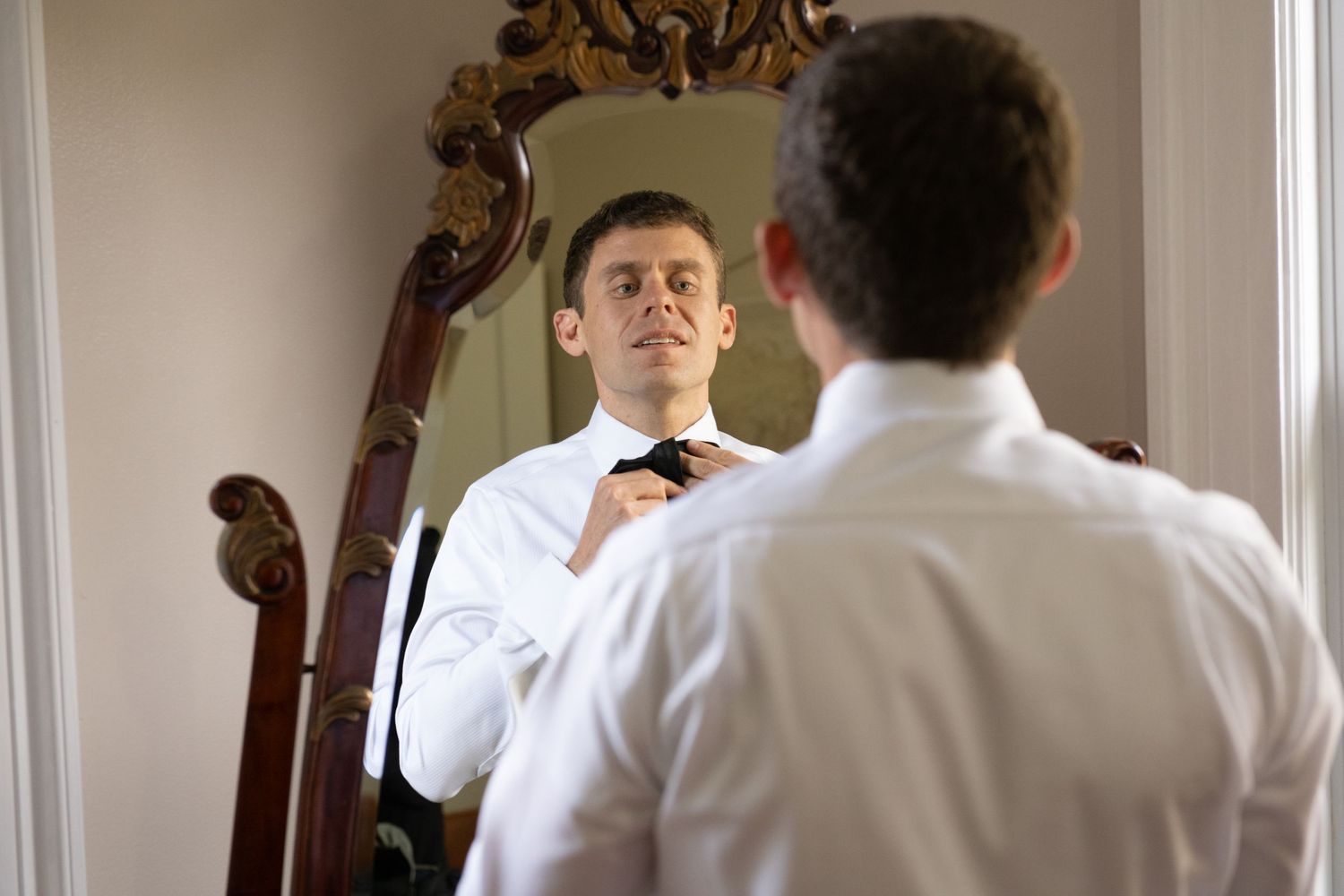Wedding party getting ready in an elegant room with ornate mirrors and white walls.