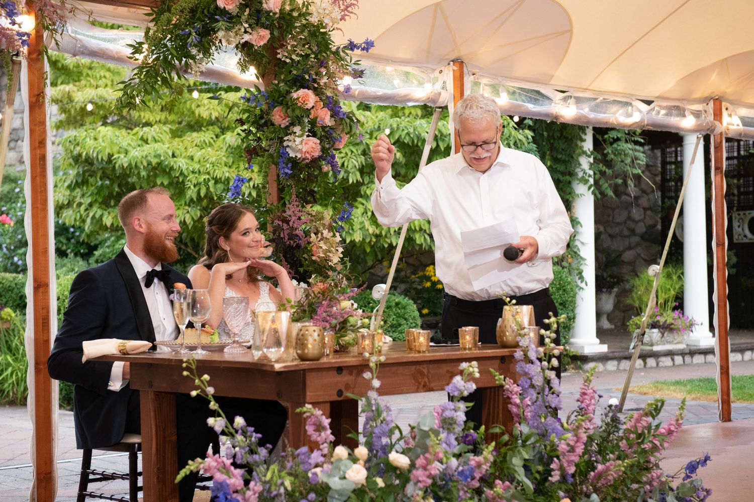 Outdoor wedding reception under a tent with floral arrangements and table settings.