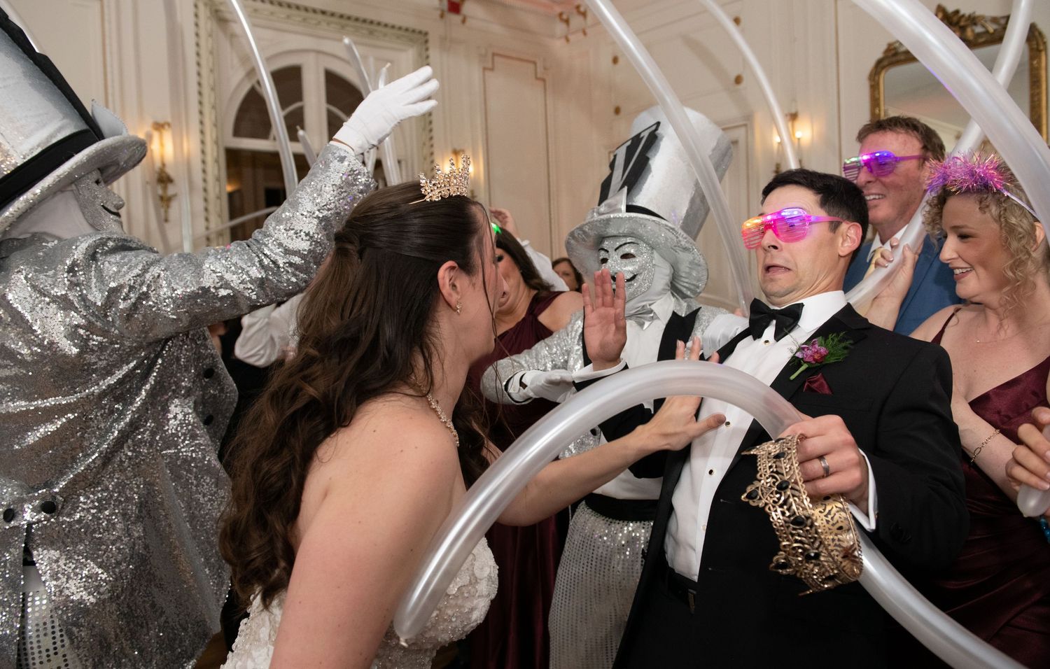 Wedding guests dancing with costumed performers in silver and white at an elegant masquerade reception.