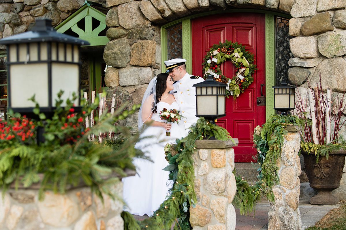 Stone archway entrance to a charming cottage with a red door and hanging flower baskets.