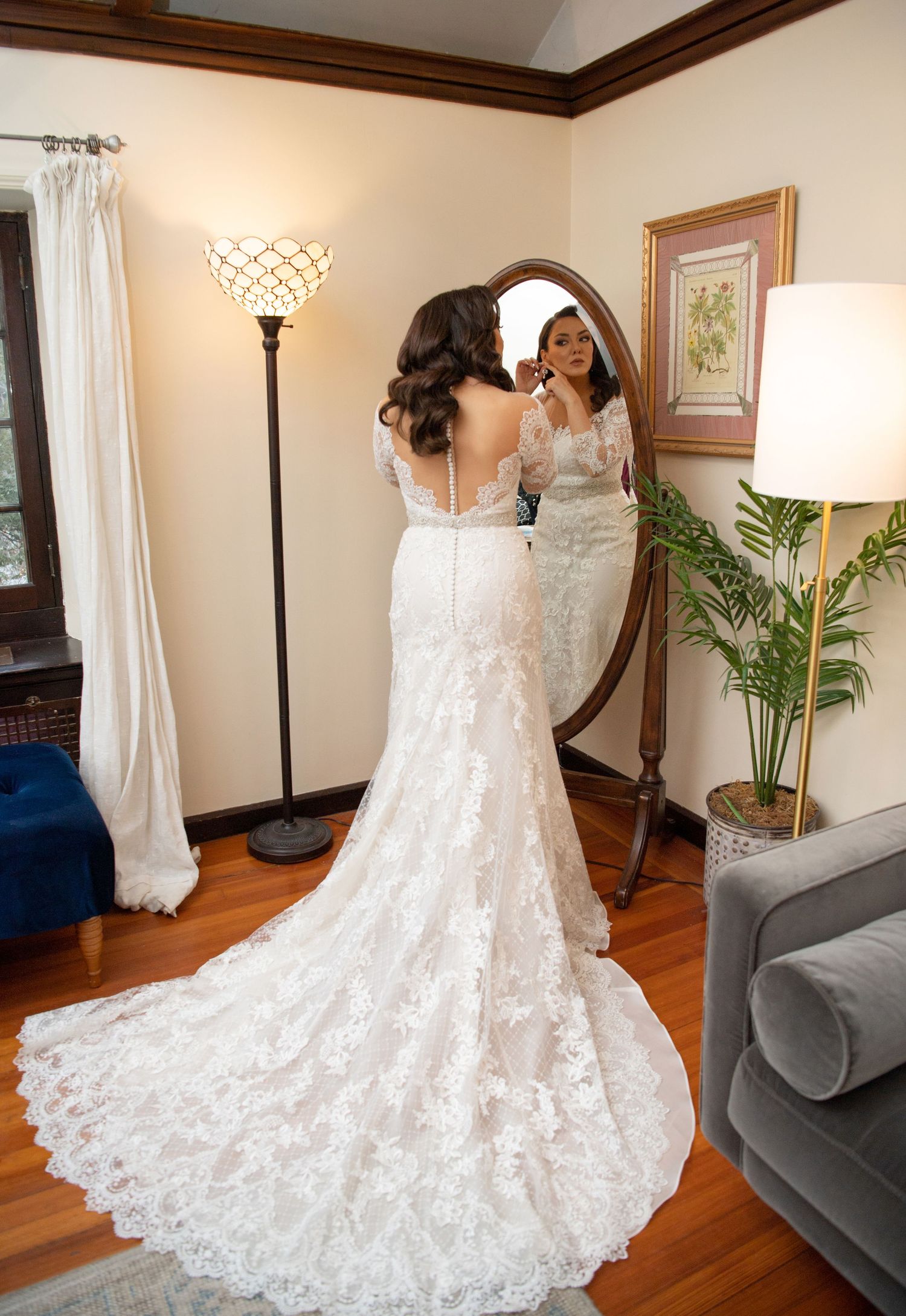 A stunning white lace wedding dress with intricate details and a flowing train displayed in a room with hardwood floors.