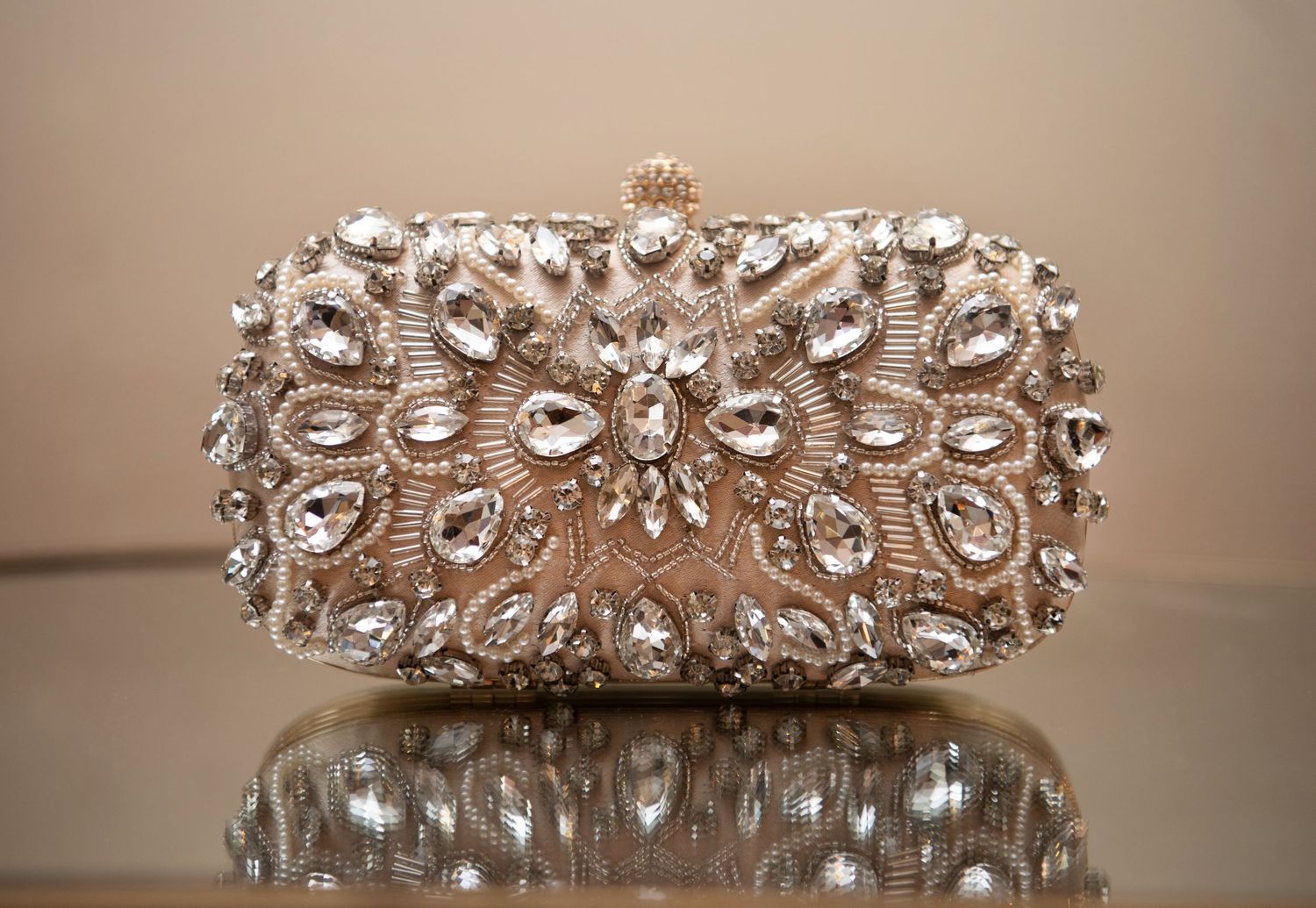 Ornate silver beaded clutch purse with crystal embellishments displayed on reflective surface.