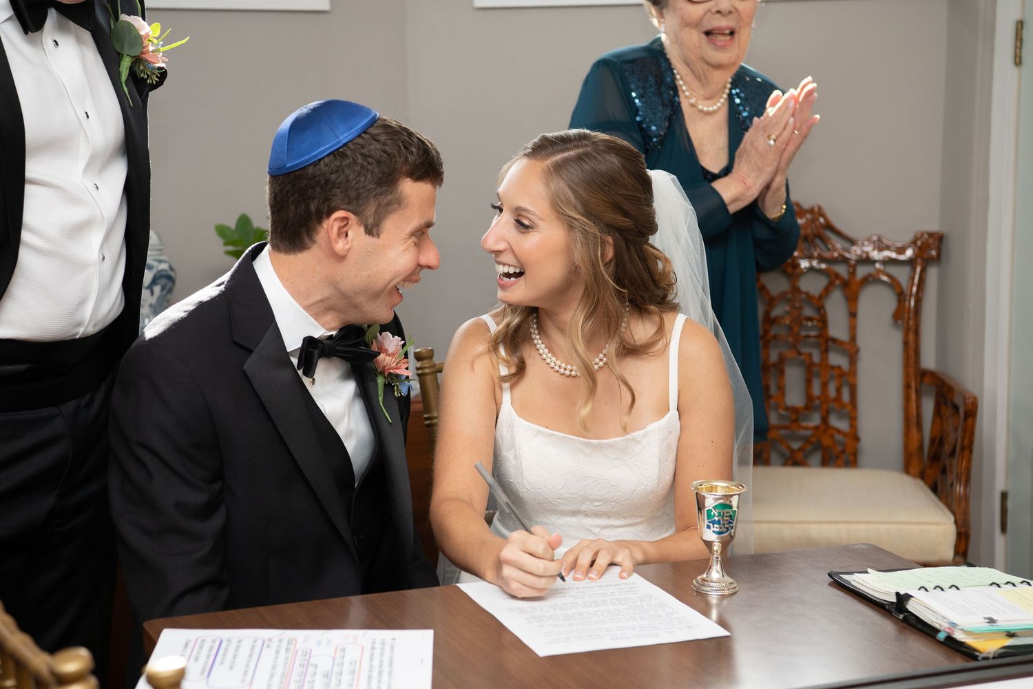 A couple shares a joyful moment while signing documents at a Jewish wedding ceremony.
