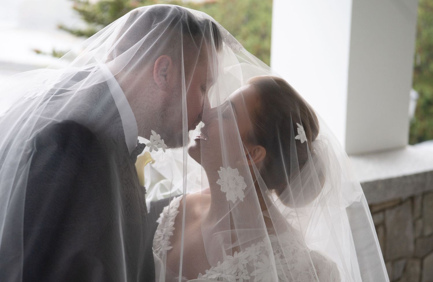 A romantic wedding moment captured under white pillars with a delicate veil flowing in the scene.